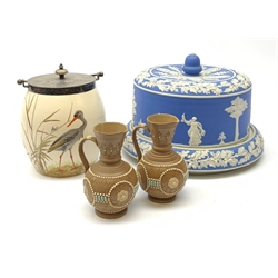 A Doulton biscuit barrel with silver plated mount and cover, hand painted with a crane amidst rushes, with painted and impressed marks beneath, including artist monogram, excluding swing handle H18cm, together with a Wedgwood or Adams style blue Jasperware cheese dome and stand, unmarked, D27cm, and a pair of Doulton Lambeth silicone ware ewers, each with impressed mark beneath, H12cm. 