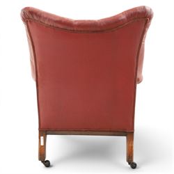 Early 20th century style oxblood red leather Chesterfield armchair, deep buttoned shaped back over padded scroll arms and loose seat cushion, raised on turned mahogany front supports with brass caps and castors