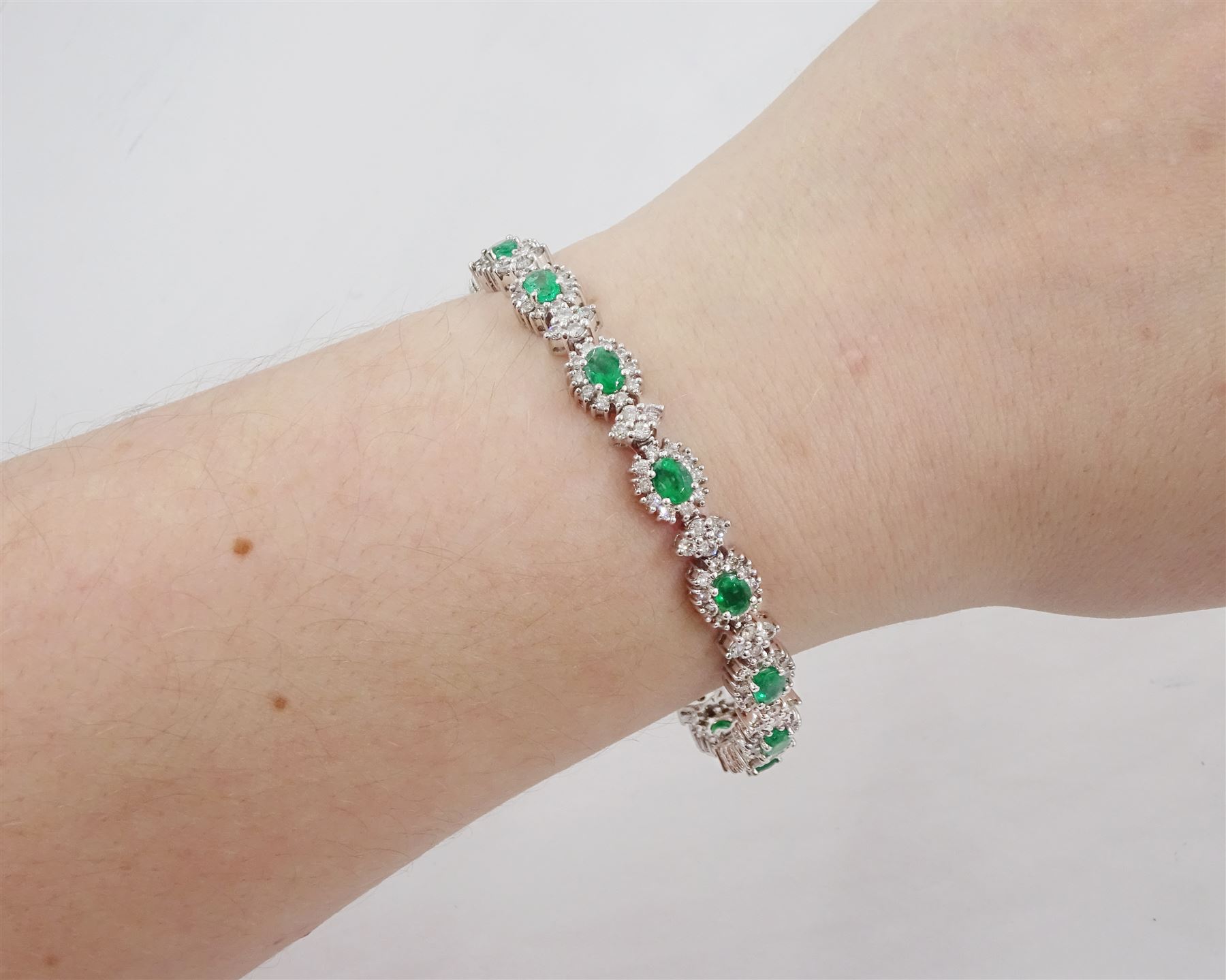 18ct white gold emerald and diamond bracelet, fifteen oval cut emeralds, each surrounded by ten round brilliant cut diamonds and spaced by a further four diamonds, stamped, total emerald weight approx 3.30 carat, total diamond weight approx 2.10 carat
