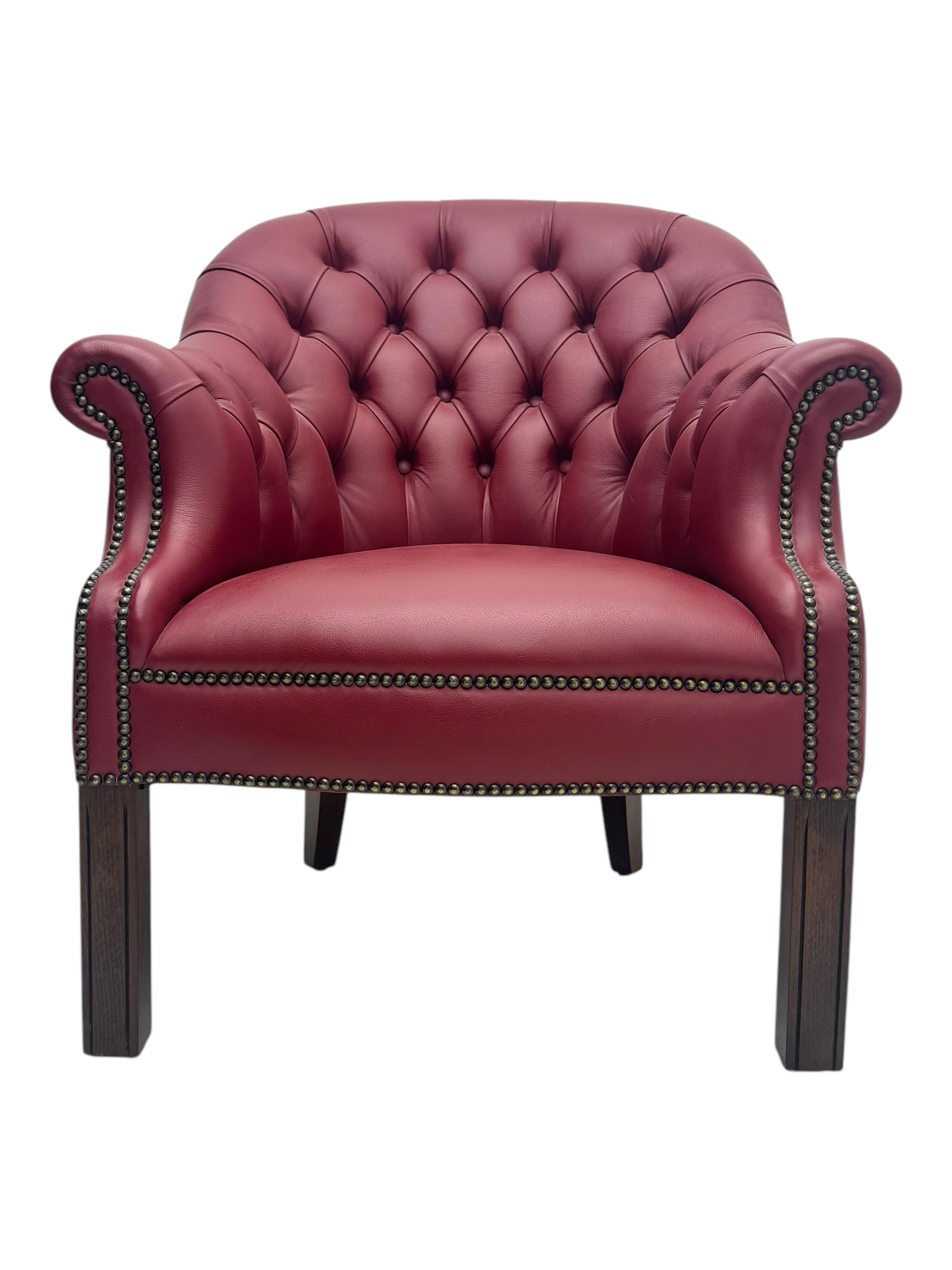 Kingsgate - contemporary 'Devon' bucket armchair, upholstered in red leather with buttoned backrest, rolled arms and brass stud detailing, raised on four dark wood supports with vertical carving