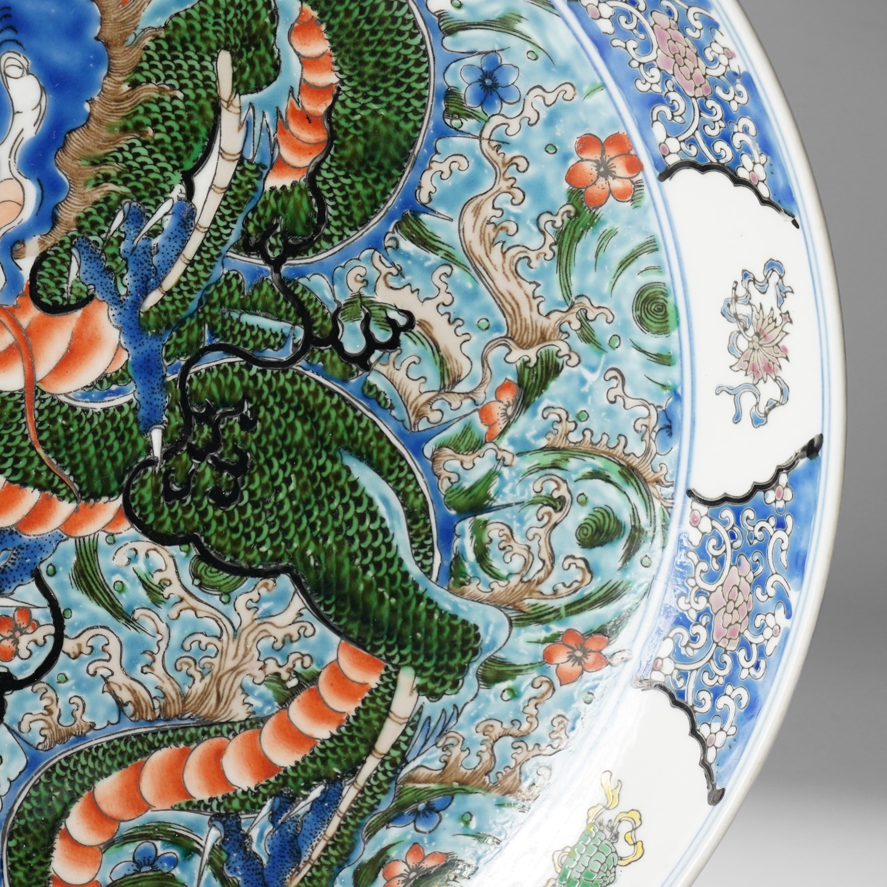 Chinese charger, decorated in blue, green and red enamels with a four clawed dragon chasing the flaming pearl amidst waves and flower heads, the rim with border of alternating reserves of auspicious emblems and flower scrolls, bearing apocryphal Kangxi mark beneath, D38cm 

