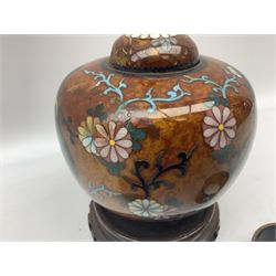 20th century Chinese cloisonné jar and cover, of bulbous form decorated with two shaped panels contained three clawed dragons, surrounded by flower heads, upon tripod feet, H13cm, with carved wooden stand, together with two cloisonné napkin rings, (3)