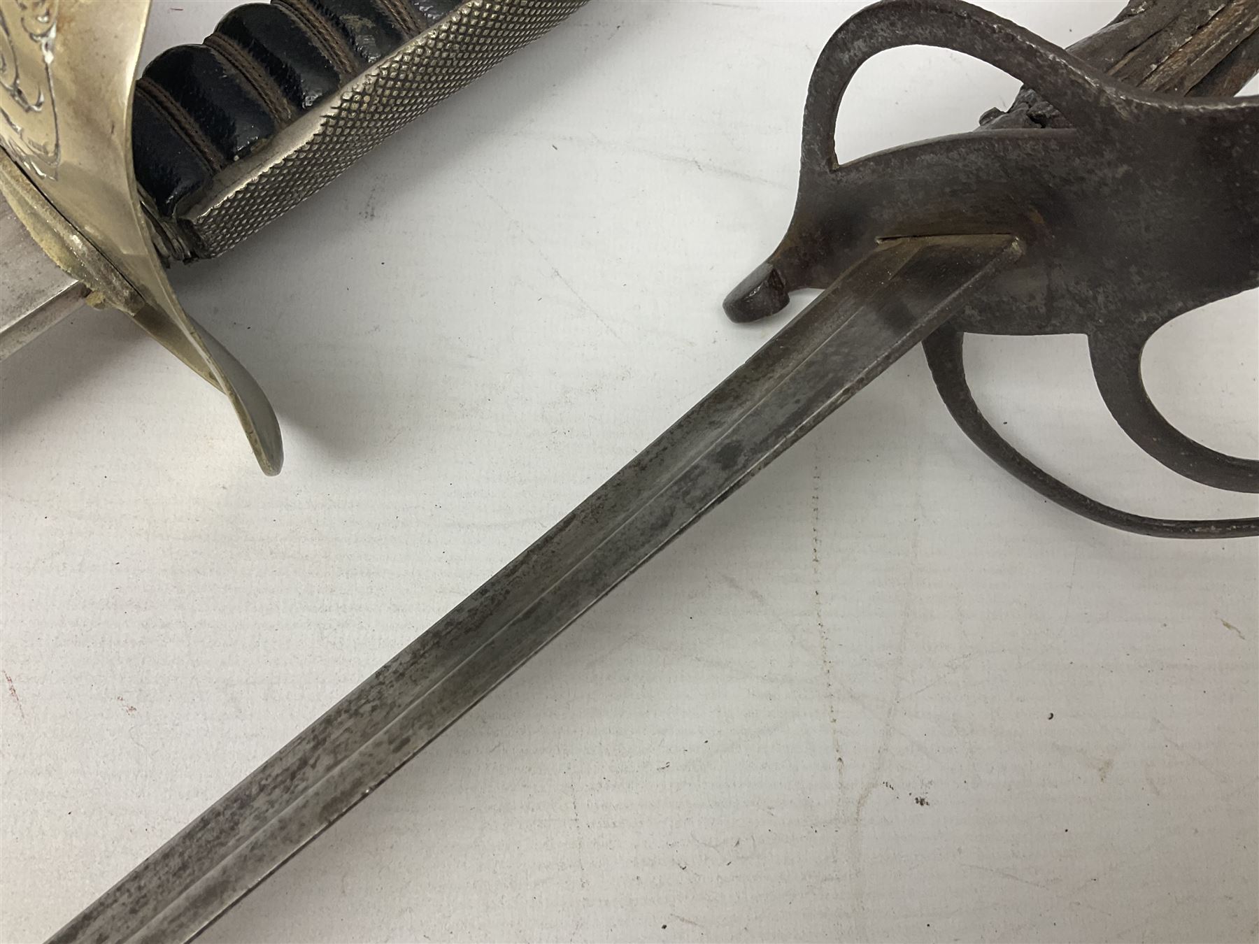 George V British Army 1897 pattern officers sword with plain 82cm fullered steel blade, pierced  basket hilt with George V cypher and wire bound leather grip with chequered backstrap; in leather covered field service scabbard L101cm overall; and another officer's sword in relic condition lacking scabbard (2)