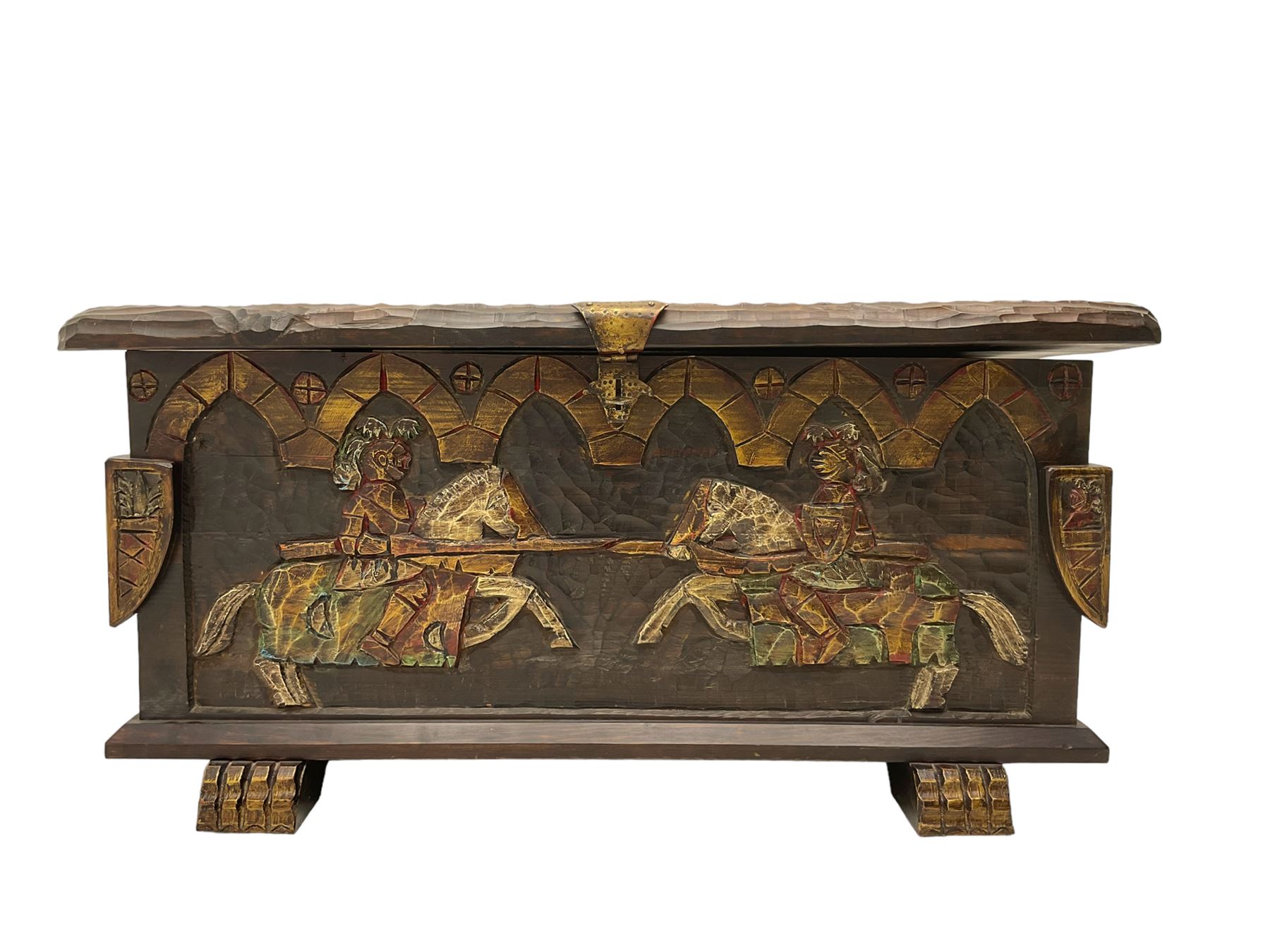 Carved wooden blanket chest, the tooled hinged lid with shaped metal strap hinges and catch, the front carved with arcade over two medieval jousters, on carved sledge feet