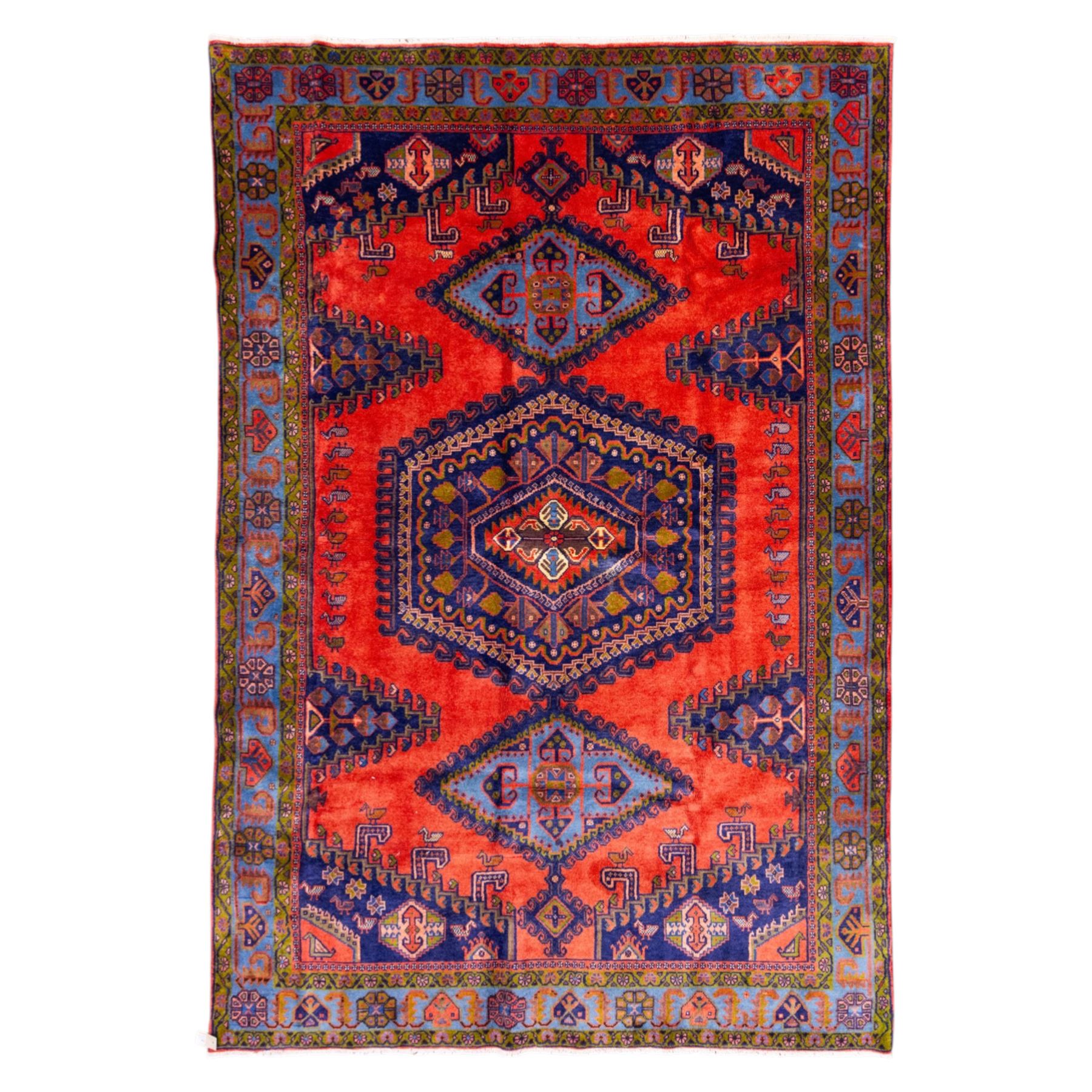 West Persian Veis hand-knotted rug, coral red field decorated with a series of bold geometric lozenge medallions in shades of indigo and sky blue surrounded by angular tribal motifs and stylized animal and plant forms framed by a deep indigo border of geometric ornament and multiple guard stripes, cotton fringe ends 
