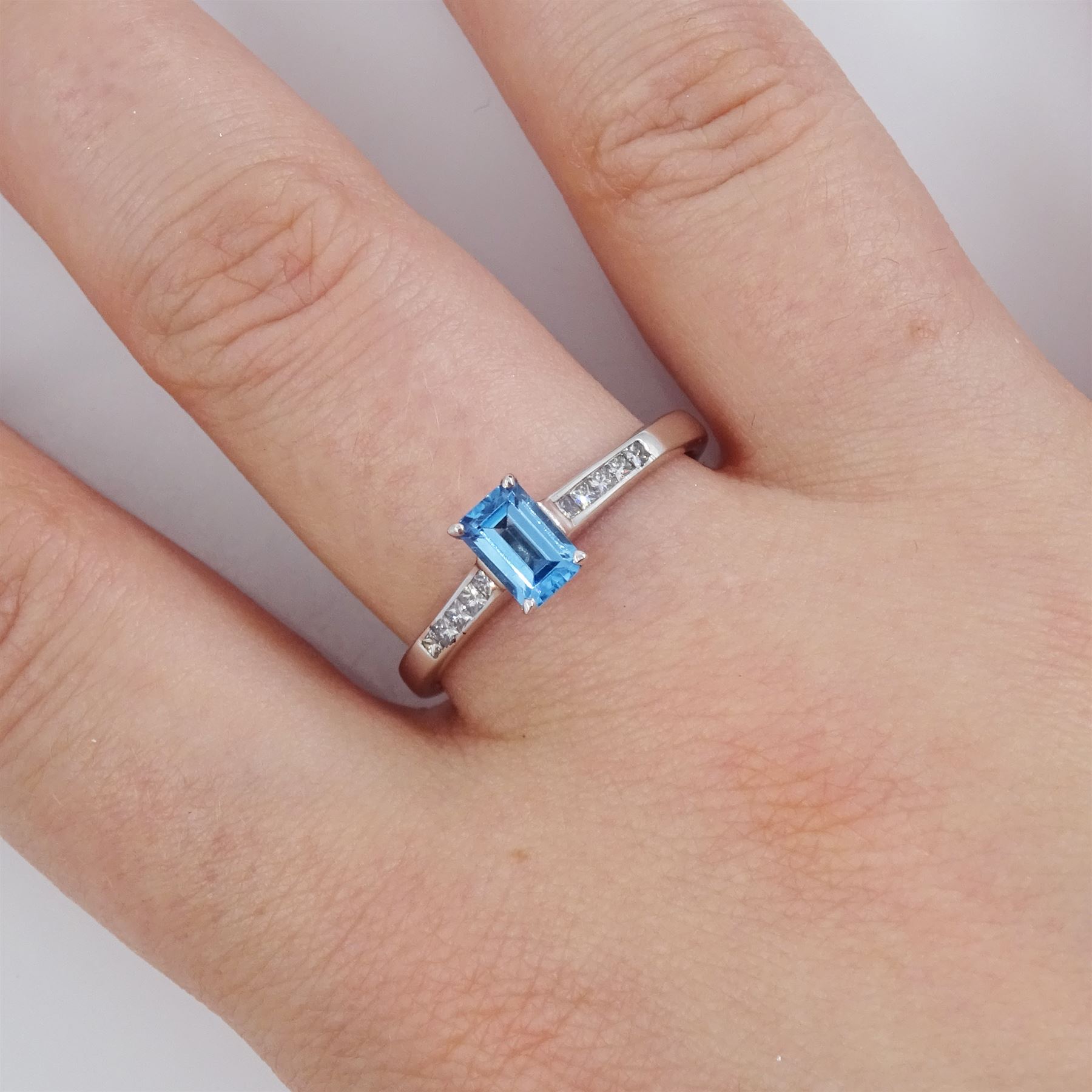 18ct white gold blue topaz and diamond ring, the single emerald cut topaz of approx 0.65 carat, each shoulder set with five, channel set princess cut diamonds