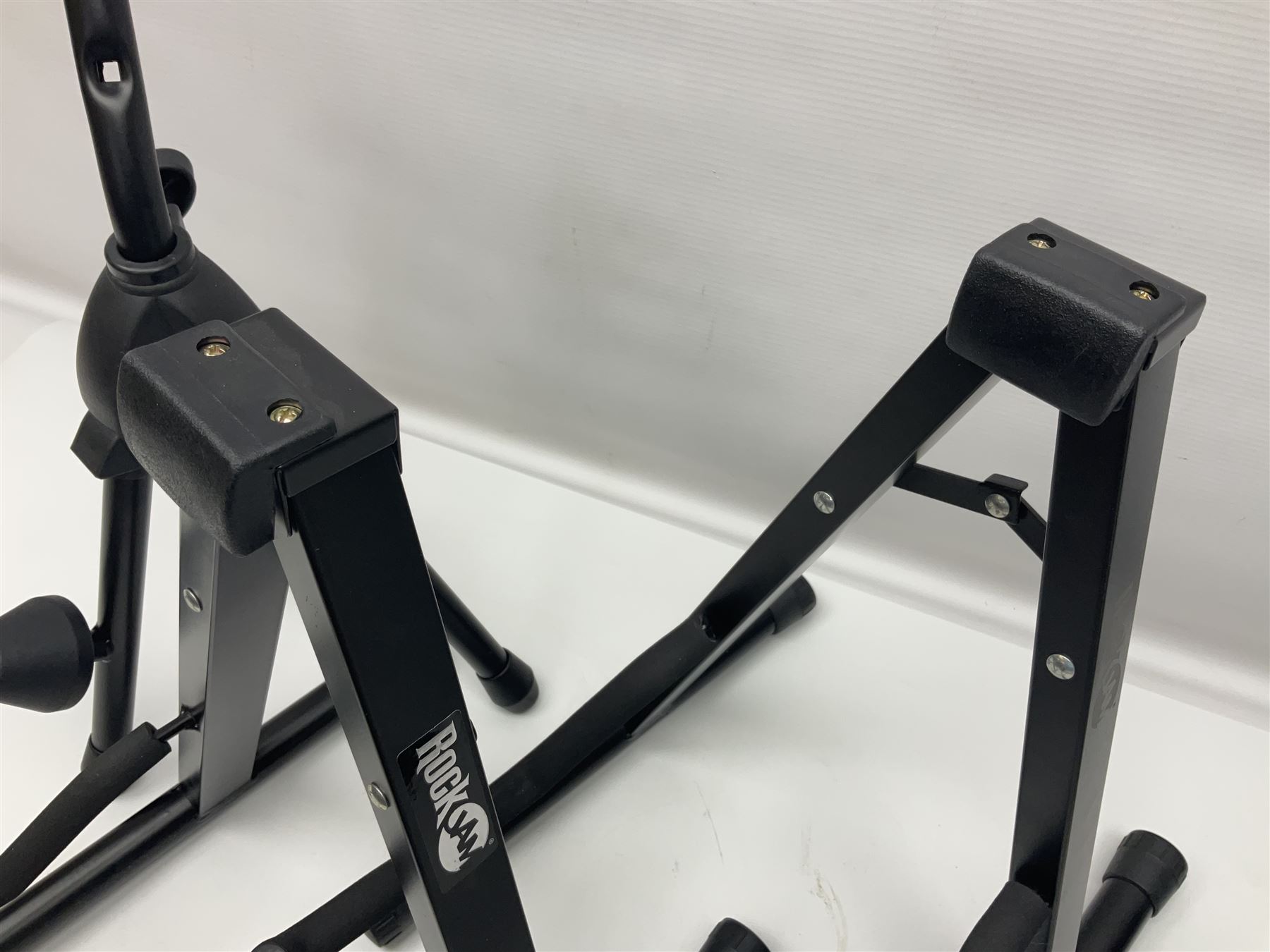Four folding tubular guitar stands, two by RockJam; and folding tubular saxophone stand (5)