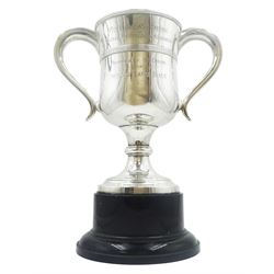 George IV silver twin handled trophy cup, the body with reeded girdle and presentation engraving, upon a knopped stem and spreading circular foot, and detachable black Bakelite plinth, hallmarked Thomas & John Settle, Sheffield 1821, overall H26cm, approximate gross silver weight (including fixtures but not plinth) 15.68 ozt (488 grams)