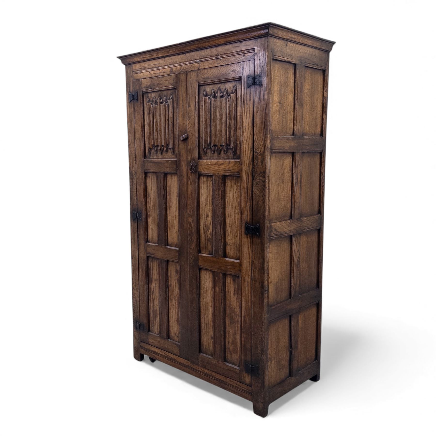 Mid 20th century oak double wardrobe, the rectangular top above twin panelled doors with carved linenfold decoration and wrought iron hinges, raised on block feet