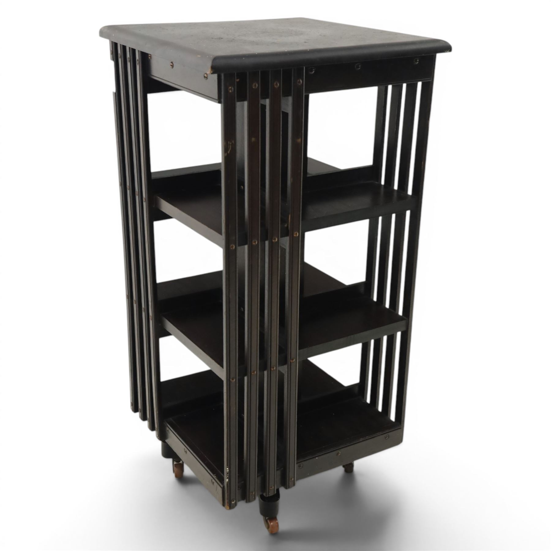 20th century ebonised revolving bookcase, square top with chamfered edges, over a three tier with four sections per tier,  revolving base on castors 