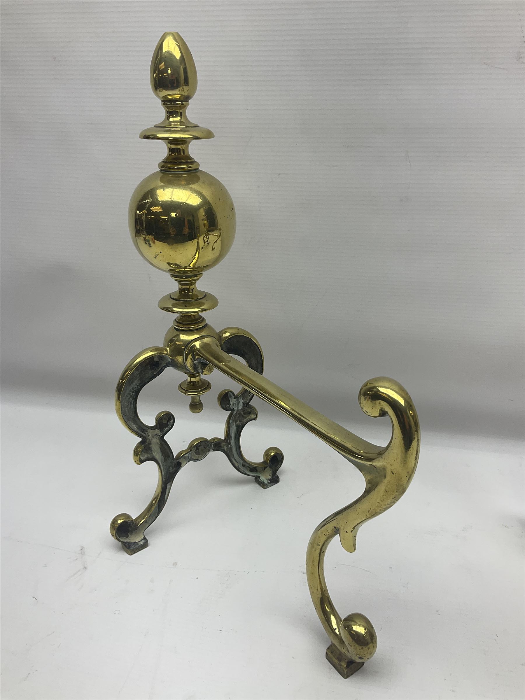 Pair of early 20th century brass fire dogs, each with sphere and urn finial, upon a scrolling base, H38cm