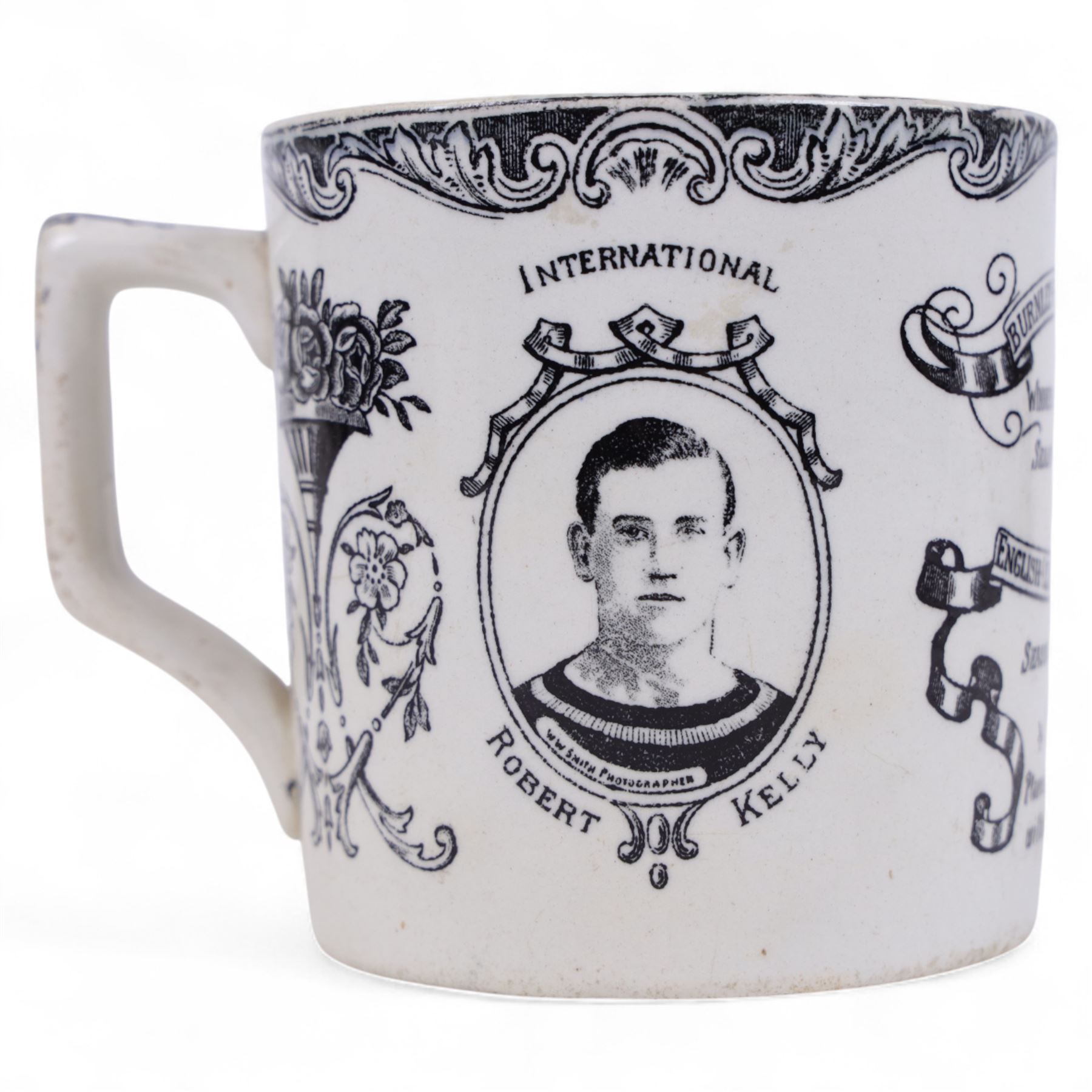 1920s transfer printed commemorative mug for Burnley Football Team English League Champions 1920-1921 season and English Cup Winners 1913-14 seson, printed in black, with portraits of Robert Kelly and 'Stick It Jerry' Dawson to the sides, bordered by scrolling and foliate decoration, H10cm