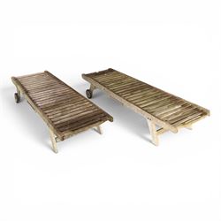 Pair of teak garden sun loungers, with slatted adjustable backrests, integrated wheels and sliding pull-out side trays, weathered natural finish.