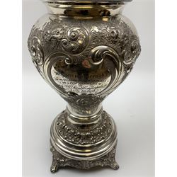 A Victorian silver plated oil lamp, of baluster form upon four scroll feet, decorated with presentation inscription within a repousse foliate and scroll surround, the collar marked Evered & Company Ltd patent safety lock collar, supporting a frosted glass shade, overall H54cm. 