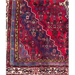 Northwestern Persian Hamadan hand-knotted rug, madder red field with a lozenge medallion enclosing an ivory centrepiece, indigo spandrels within an ivory border of stylized floral motifs between multiple guard borders 