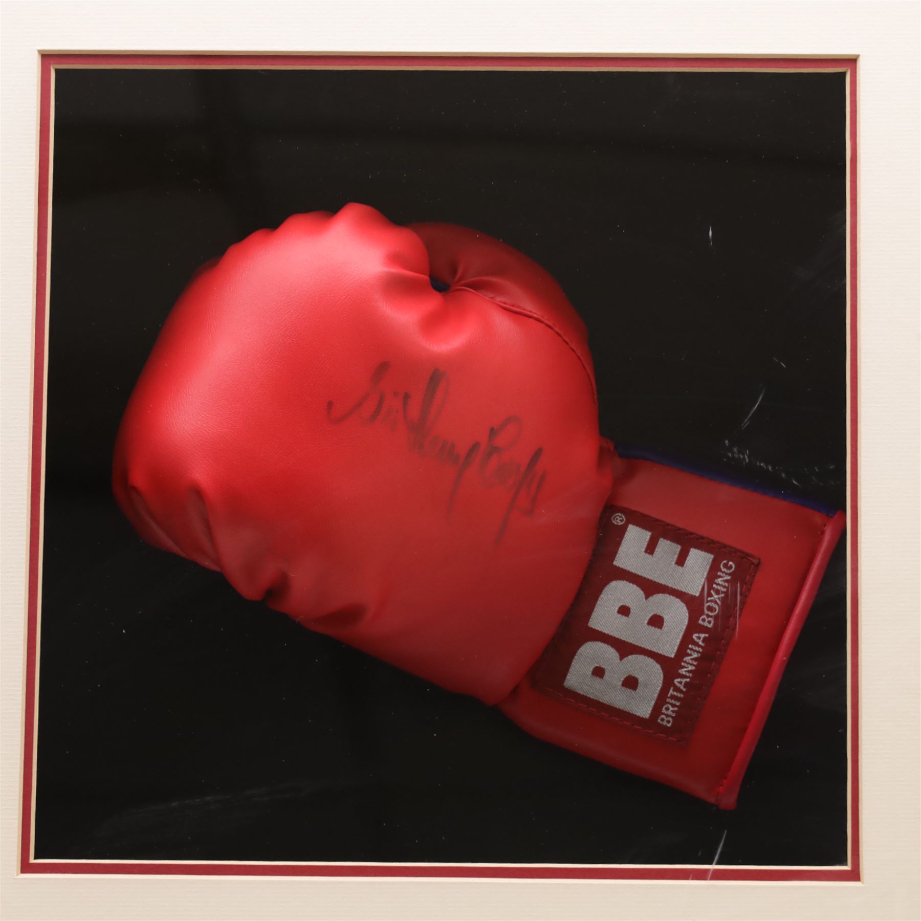 Framed display contained a single BBE Britannia boxing glove, signed by Sir Henry Cooper, displayed with a black and white print of Cooper with Ali on the ropes, with certificate of authenticity by Superstars For You, frame H59cm