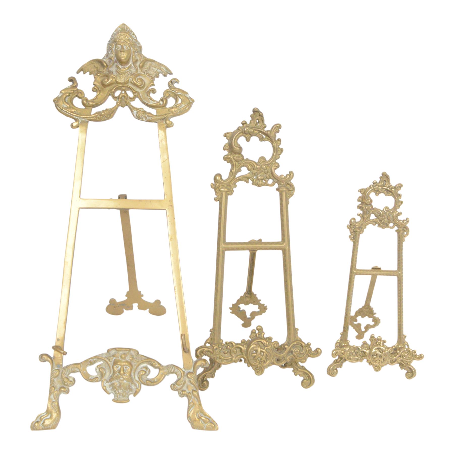 Three Baroque design brass table easels, the largest with cast mask detail, H47cm, and two matched graduated examples, smallest H25cm