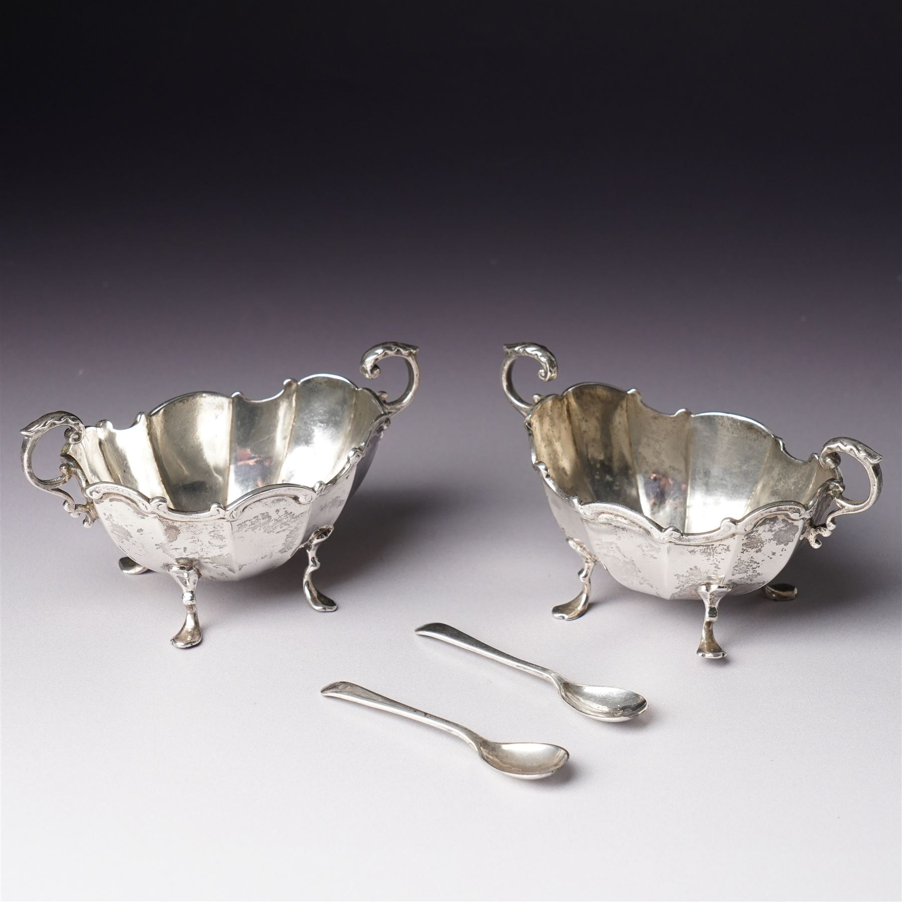 Pair of late Victorian silver salts of oval panel sided design with scroll handles and shaped supports Birmingham 1899 Maker Henry Matthews and two later silver salt spoons 
