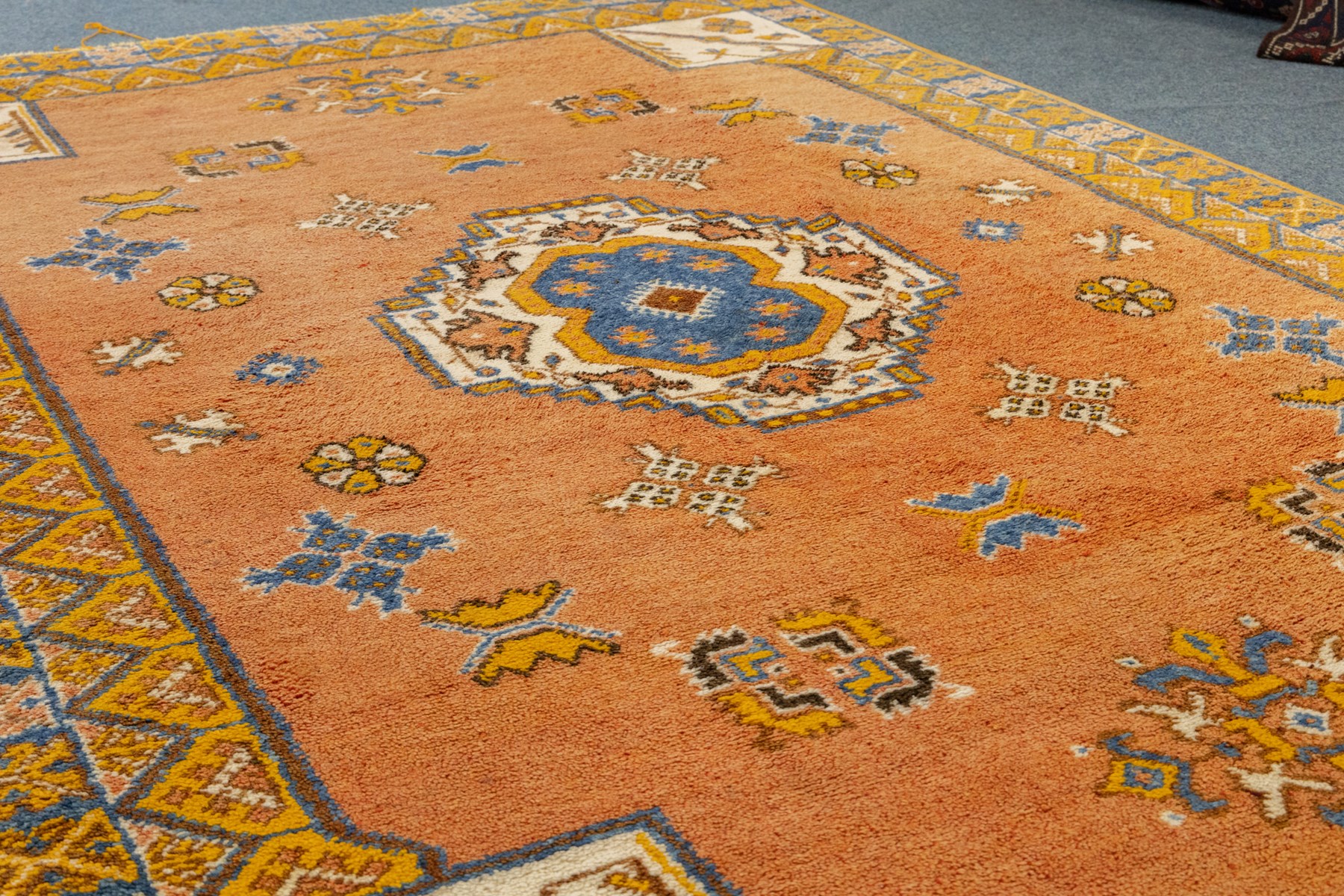 Turkish Anatolian hand-knotted carpet, salmon ground centred by a blue and cream octagonal medallion, scattered with geometric floral and tribal motifs, cream spandrels and yellow geometric border