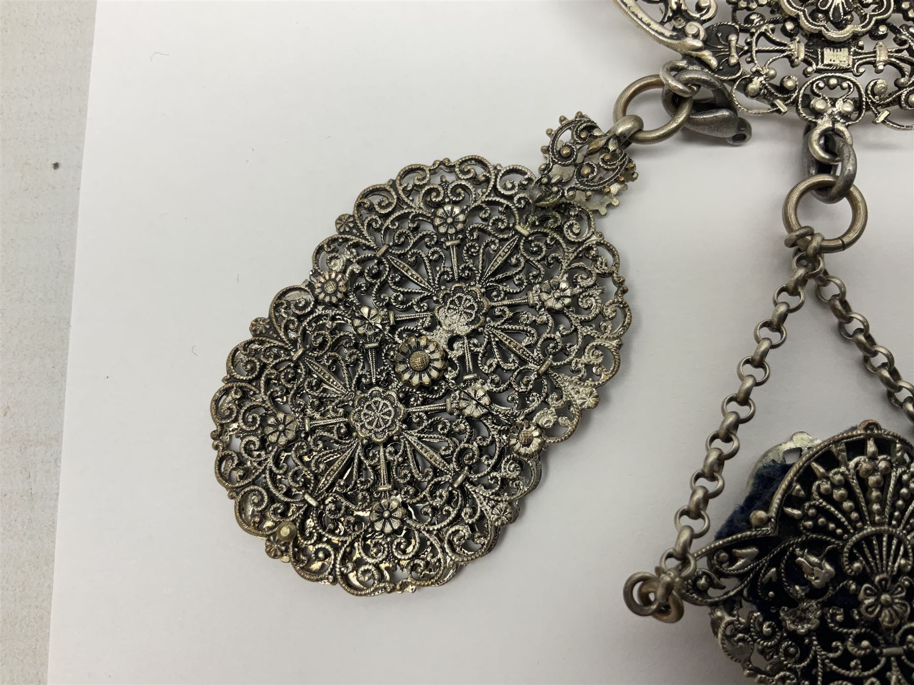 19th century continental silver plated chatelaine, the main body flanked with winged mythical beasts and central soldier slaying a dragon supporting three suspended items to include velvet lined small basket and long clasped filigree chain, together with a thimble