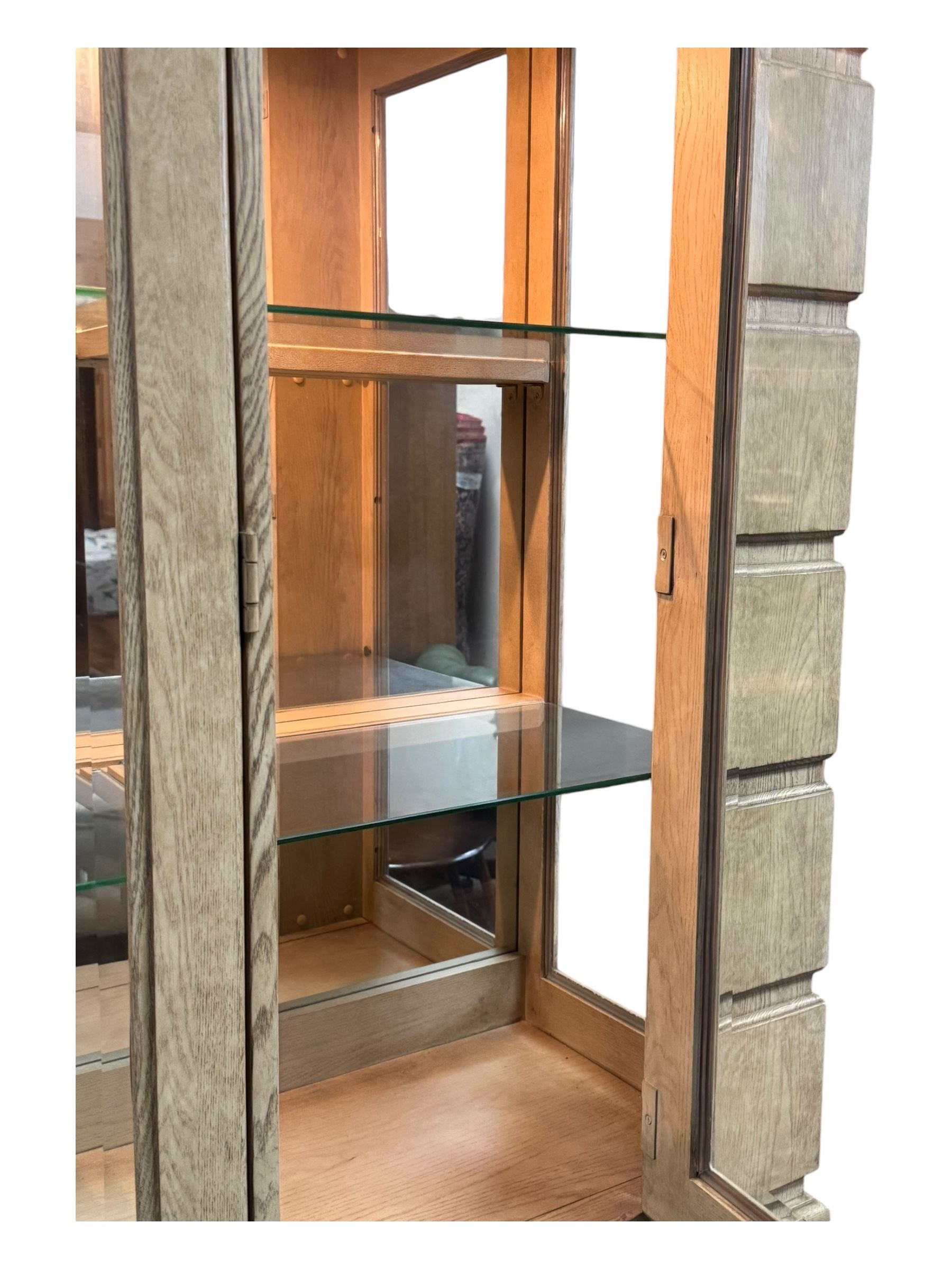 Brunswick - washed oak finish illuminated display cabinet, upper section with four glass-panelled doors enclosing glass shelving, base fitted with two drawers over four paneled cupboard doors, each fitted with distinctive round metal handles, raised on plinth base