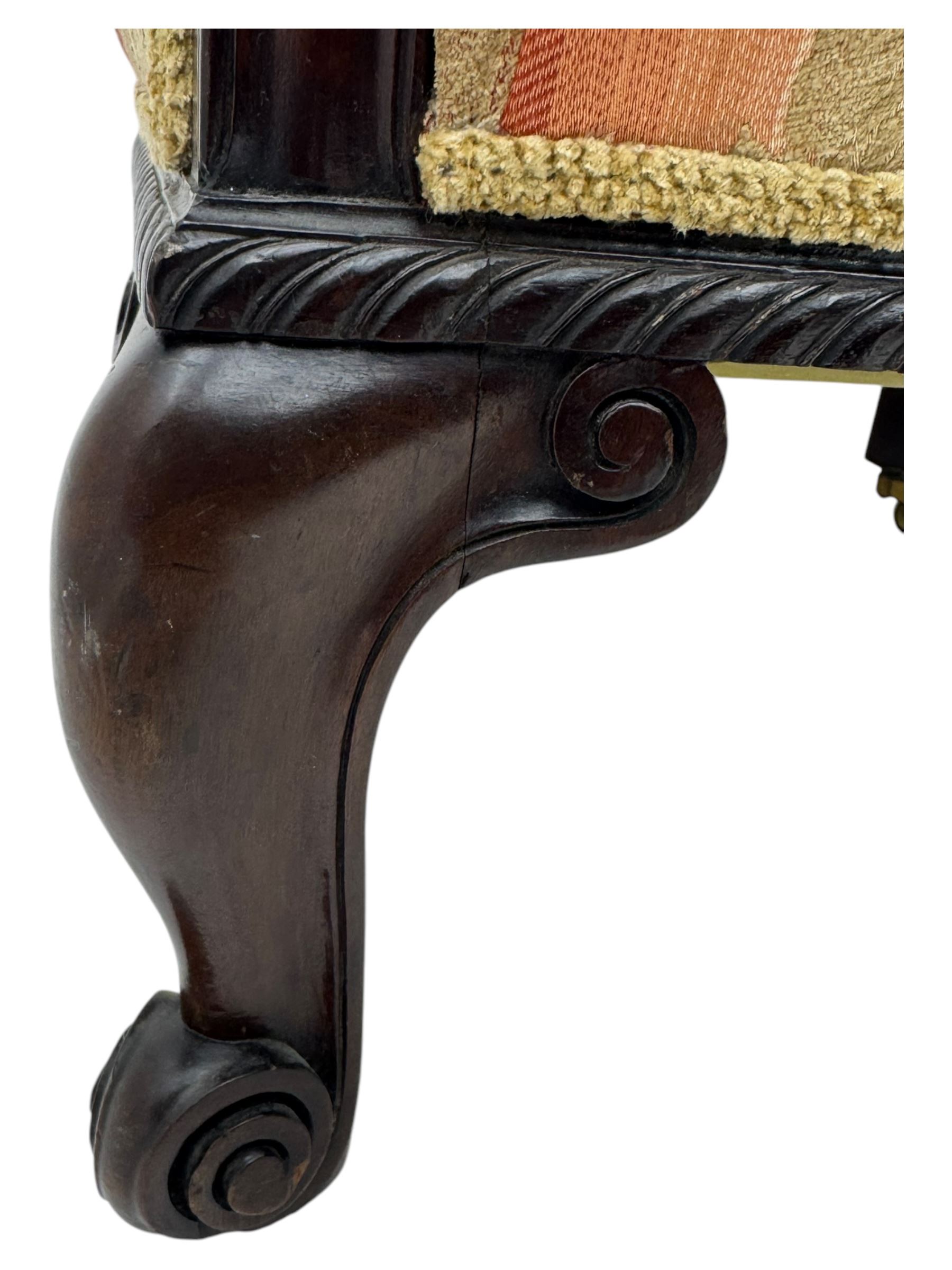 Early 20th century mahogany framed upholstered tub armchair, scrolled arms, upholstered in a damask-style fabric with foliate pattern, raised on cabriole front legs upon brass castors