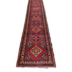 Persian Hamadan runner, red ground, decorated with eighteen lozenge medallions decorated with stylised floral motifs, three band border decorated with plant motifs and geometric patterns
