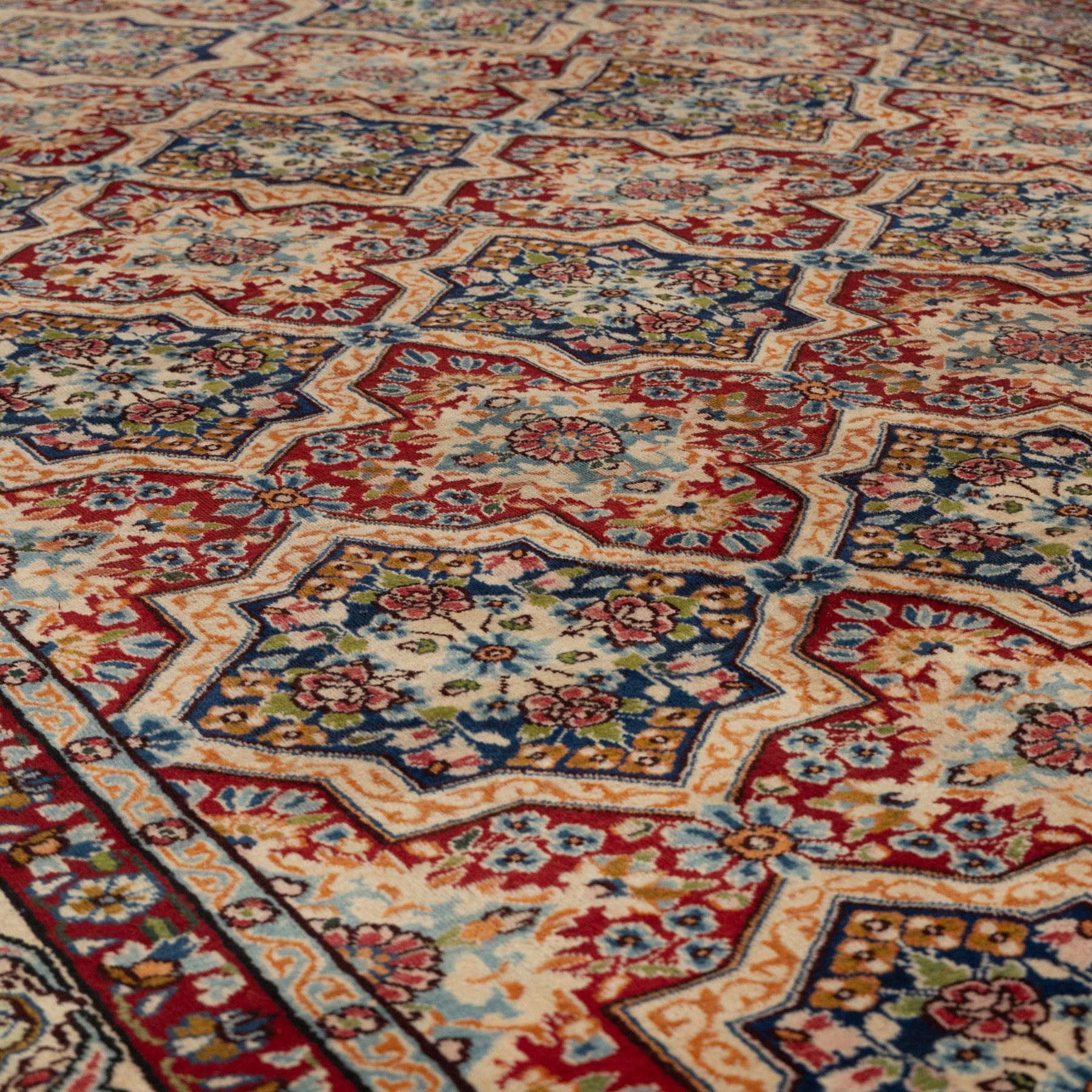 Central Persian Kirman carpet, the field arranged with alternating indigo star shaped and red cruciform compartments, each filled with rosettes, flowerheads and scrolling foliage, enclosed by a broad ivory palmette border and red floral guard bands