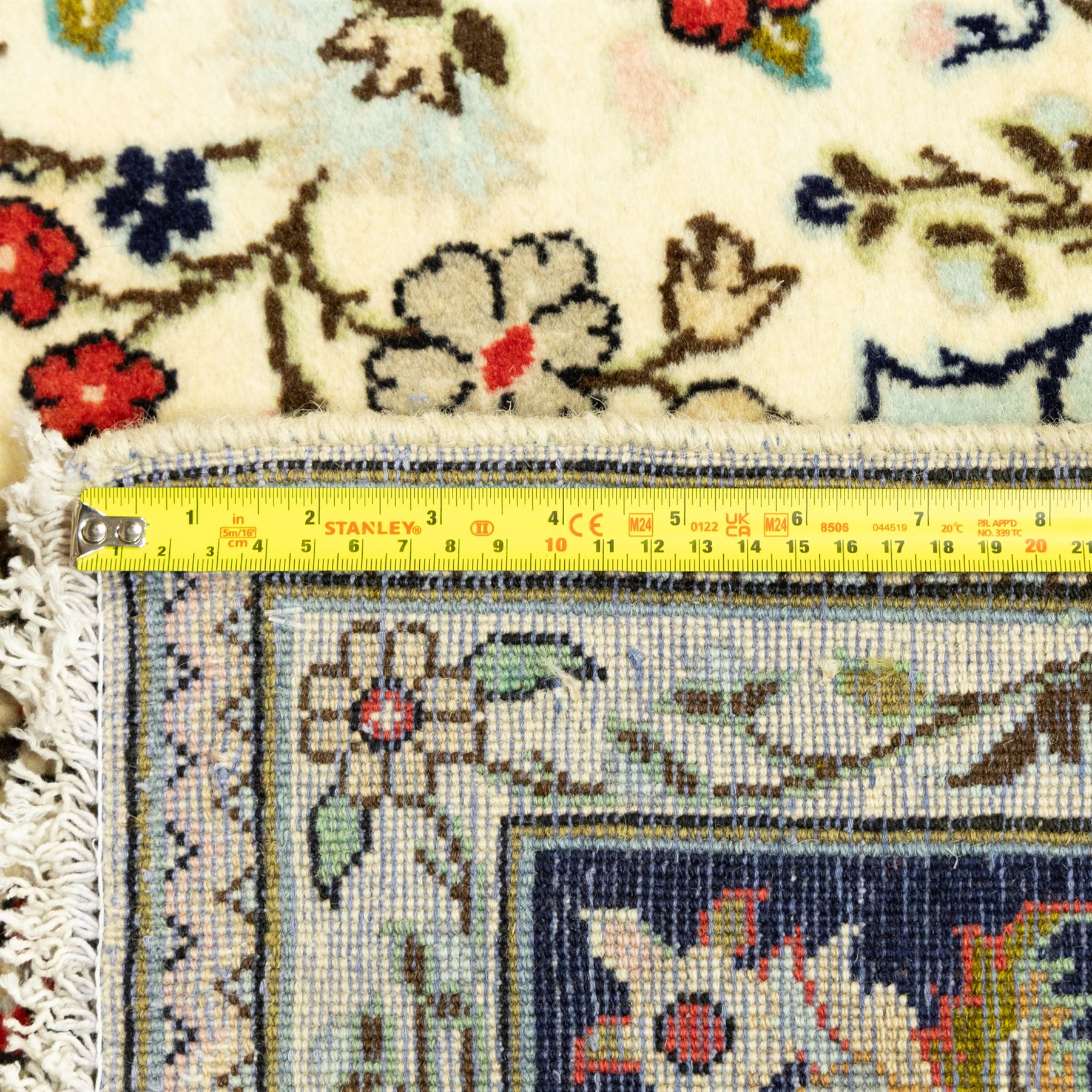 Central Persian Kashan hand-knotted carpet, ivory ground, with an all-over floral field centred by a subtle shaped medallion, surrounded by scrolling foliate and floral motifs incorporating rosettes, palmettes and delicate vine work, enclosed by a dark navy border with repeating palmettes and meandering vines, flanked by floral guard stripes, with cotton fringes