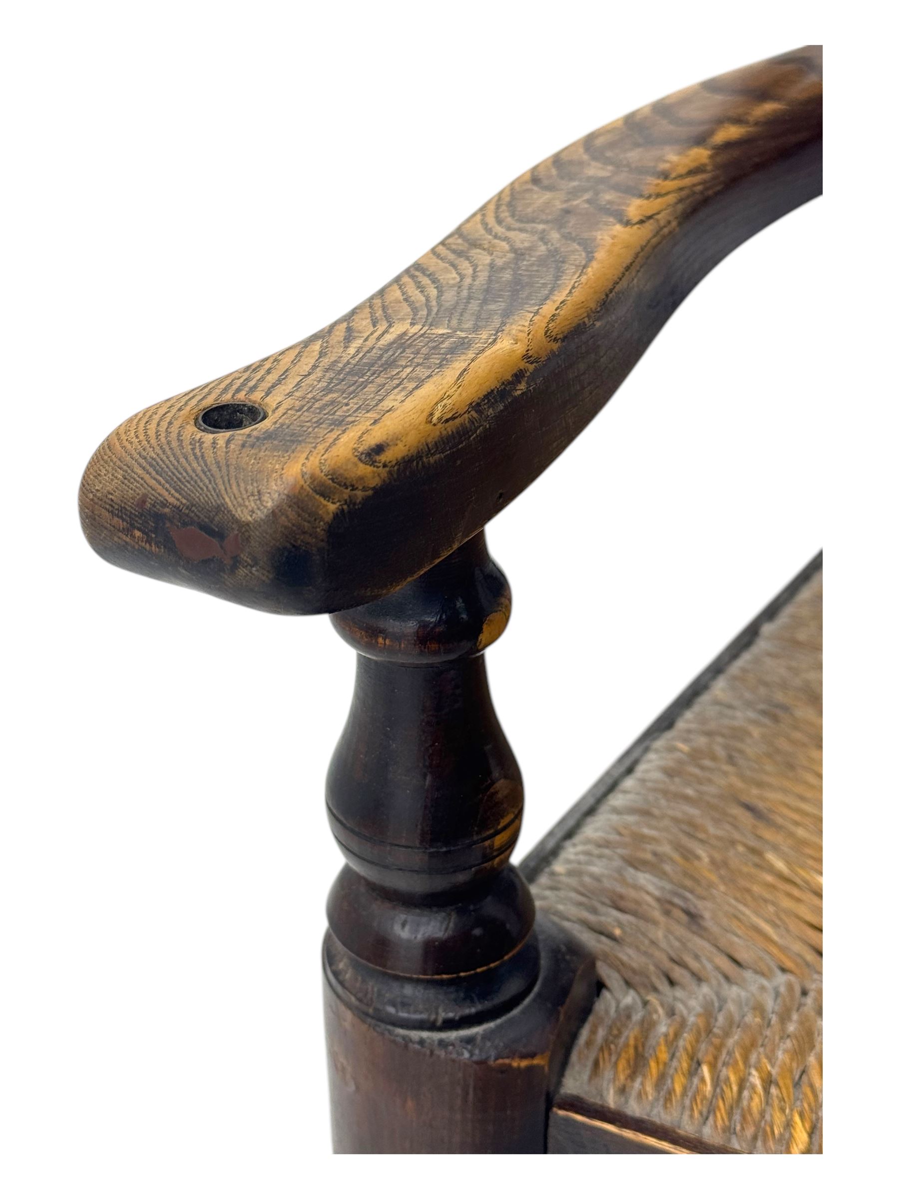 Early 19th century ash armchair, the back with winged spindles extending from a shaped top rail, above a splat of two rows of vertical spindles, with curved arms and a rush seat, raised on turned supports united by double stretchers terminating in castors