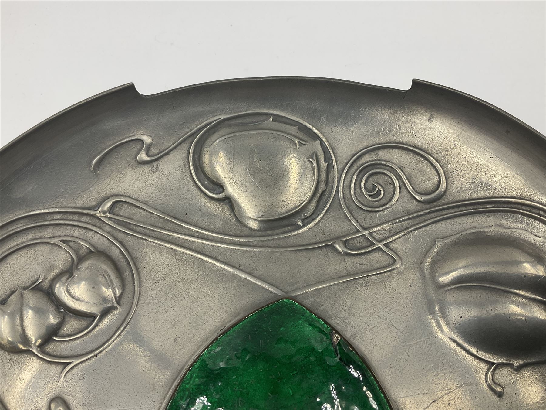 Liberty & Co Tudric pewter Bollelin tray, designed by Archibald Knox, of circular form with shaped edge, cast in relief with foliate tendrils surrounding a green enamel cartouche, impressed beneath Made by Library & Co English Pewter 044, D25.5cm