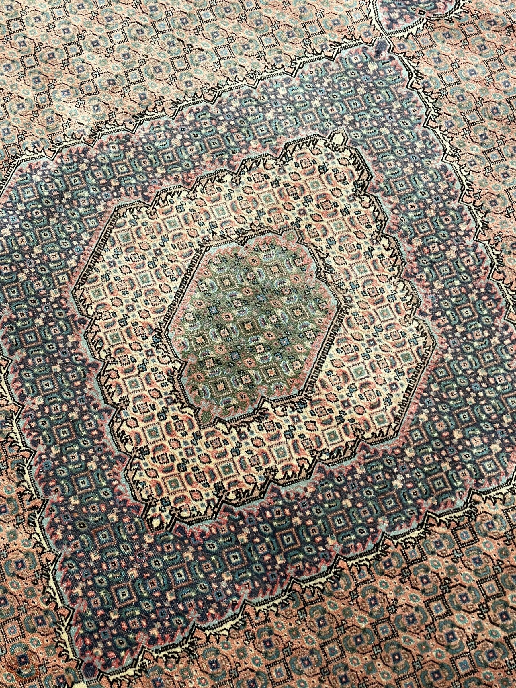 Persian Bidjar peach ground carpet, central pole medallion enclosed within lozenge field and spandrels, decorated all over with small Heratti motifs, the main border with trailing pattern decorated with stylised plant and Boteh motifs, within two triple band guard stripes with repeating flower head decoration 