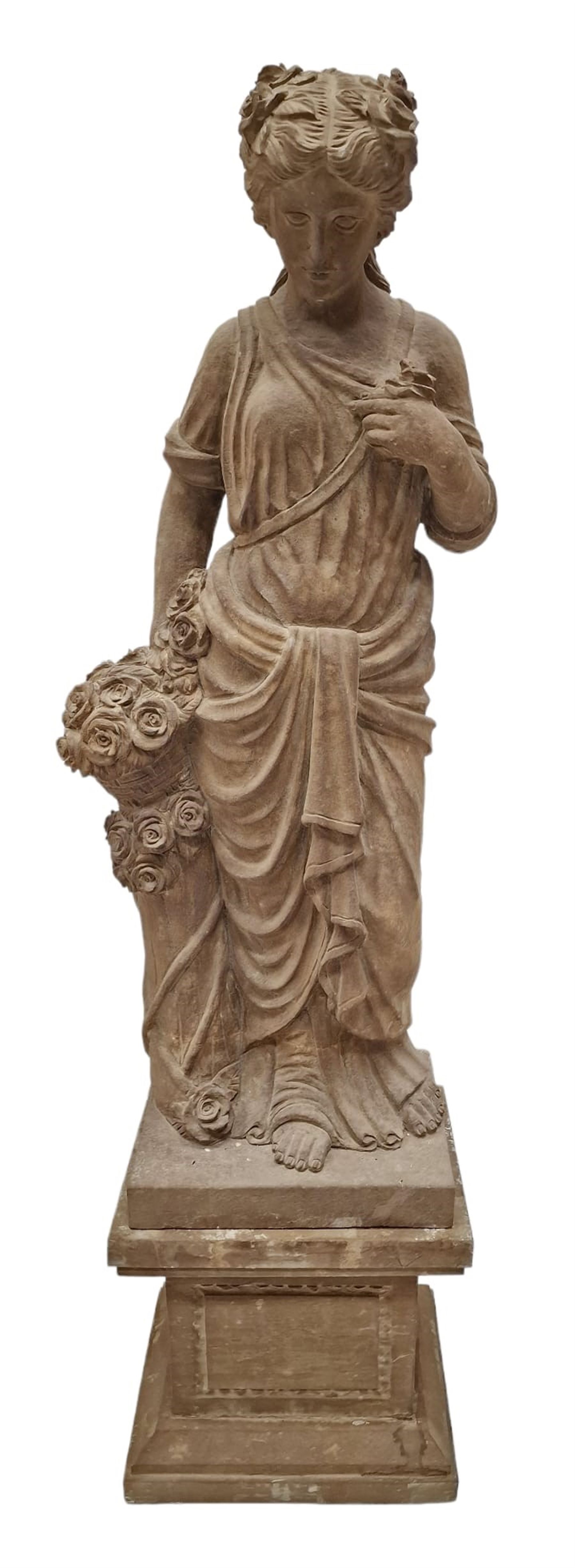 Hand carved stone Neoclassical figure of the Roman goddess Flora, her hair pinned with roses, draped in a toga, holding a basket of flowers in her right hand, raised on a stepped square plinth base 