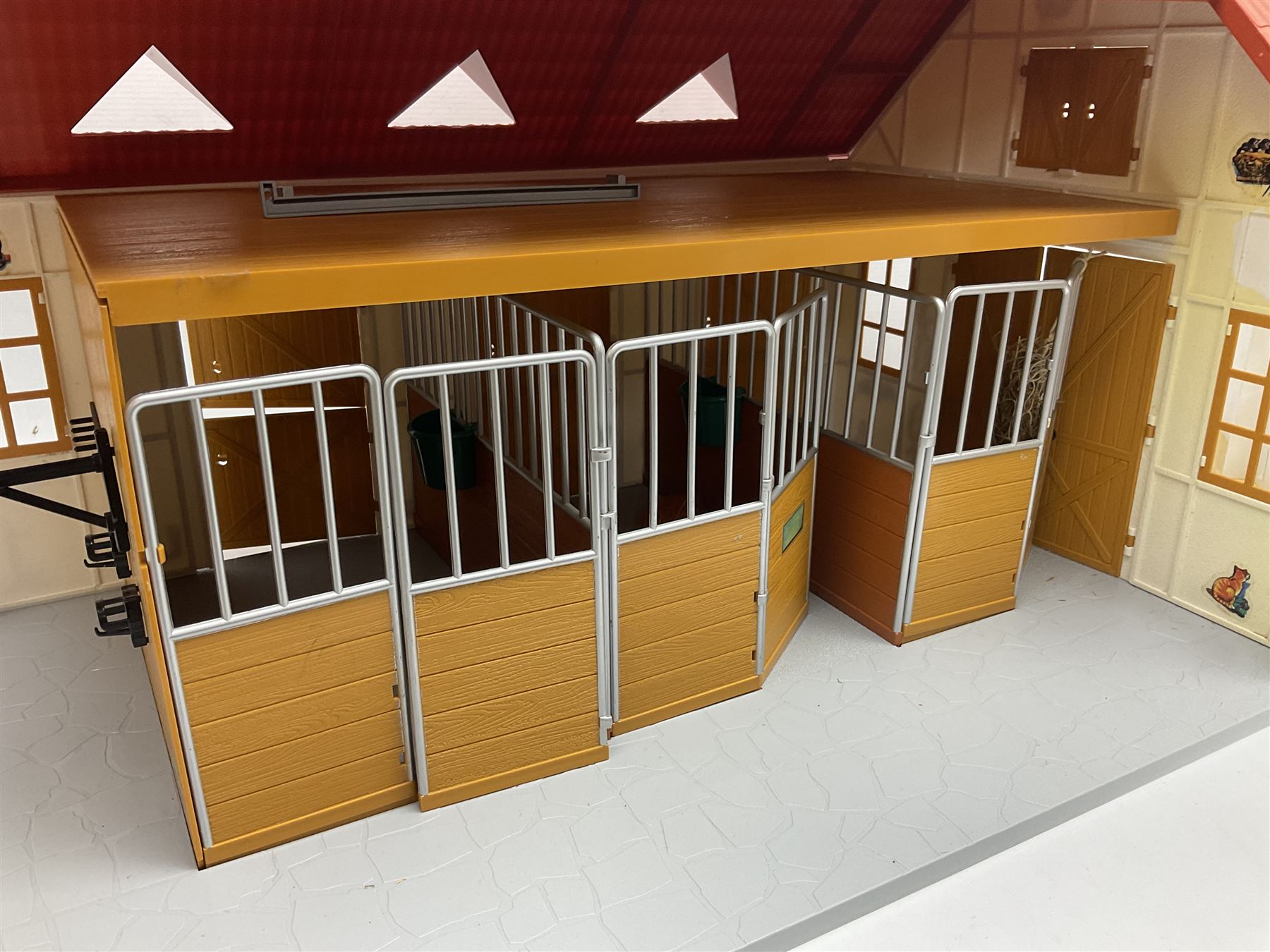 Sectional wooden horse stables playset by Julip with two stalls and tack room under a pitched roof, base 59 x 47cm; and another sectional plastic stables playset by Schleich with three stalls under an open pitched roof, base 56 x 36cm (2)
