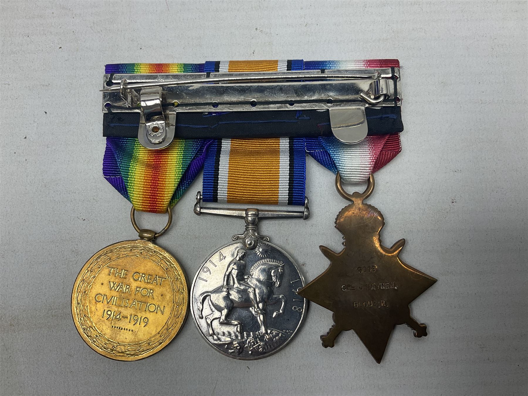 WW1 KIA group of three medals comprising British War Medal, 1914-15 Star and Victory Medal awarded to 9069 Cpl. J. Mayhew Glouc. R.; with ribbons; displayed on modern bar, and photograph of recipient in uniform; some biographical details