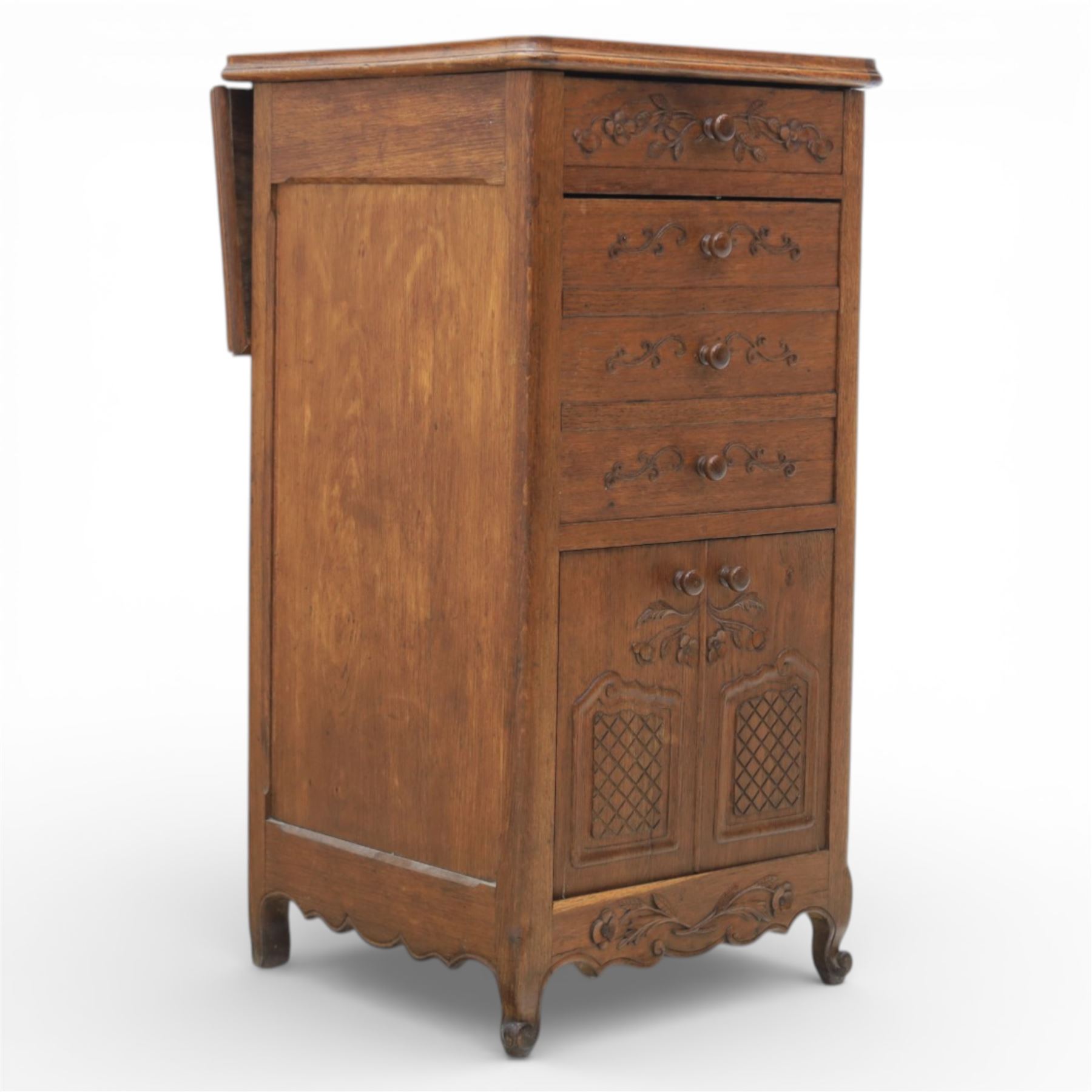20th century French style oak bedside chest of pedestal form, the top with rounded moulded edge with drop leaf to the back, above five carved drawers with applied scroll ornament and turned knobs, the cupboard base with twin carved doors with diamond lattice panels, with shaped apron and bracket feet