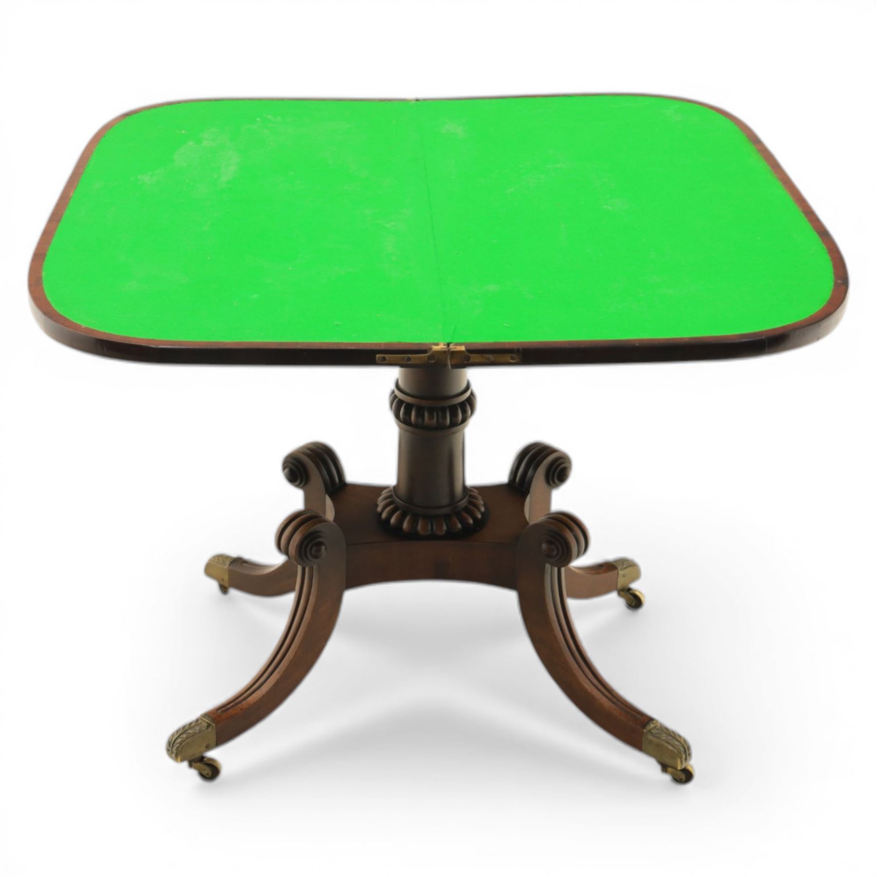 Early 19th century Regency mahogany fold over card table, the rounded rectangular top with brass line inlay enclosing green baize playing surface, crossbanded and strung exterior, with reeded edge above a gadrooned frieze, raised upon a turned column and four reeded sabre supports terminating in brass caps and castors