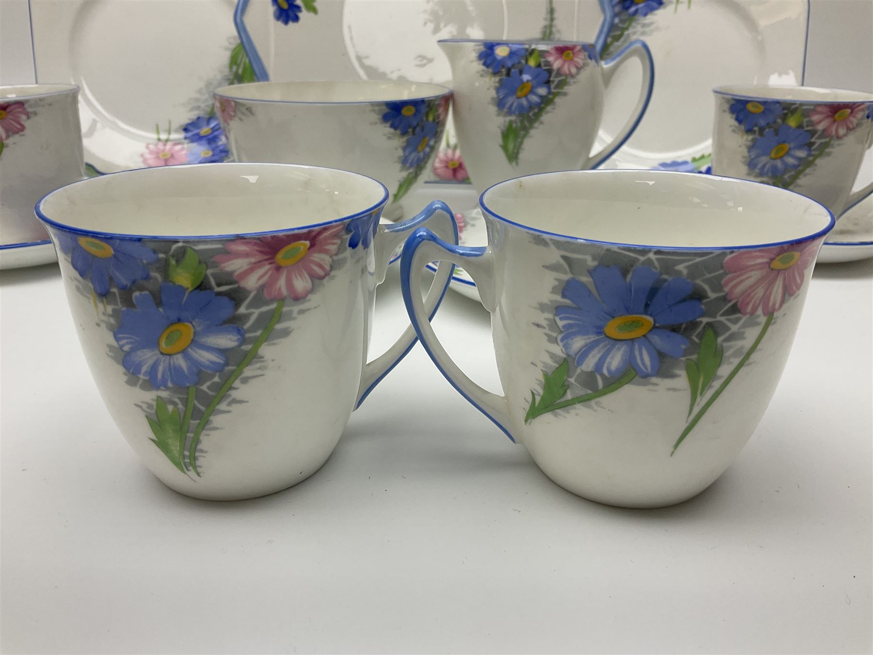Shelley Strand shaped tea wares, decorated with blue and pink daisies upon a white ground, comprising four teacups, four saucers, three tea plates, milk jug, sugar bowl and cake plate, all with printed green mark beneath and painted pattern no 12216