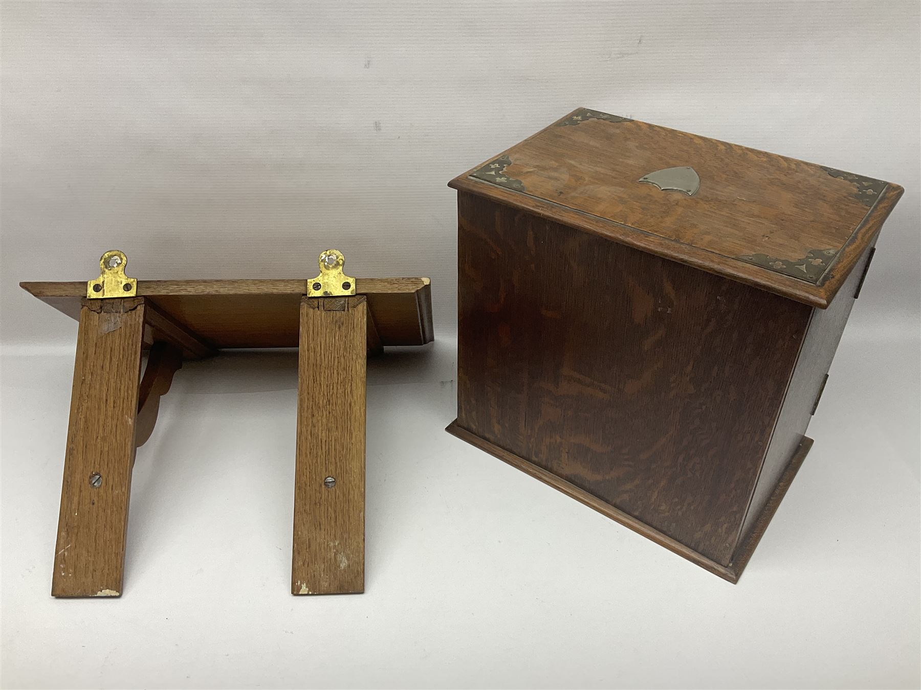 Early 20th century oak smokers cabinet, with brass shield shaped mounts, opening to reveal a compartmentalised interior with three drawers, pipe rack and tobacco jar, together with a small wooden shelf, smokers cabinet H28.5cm