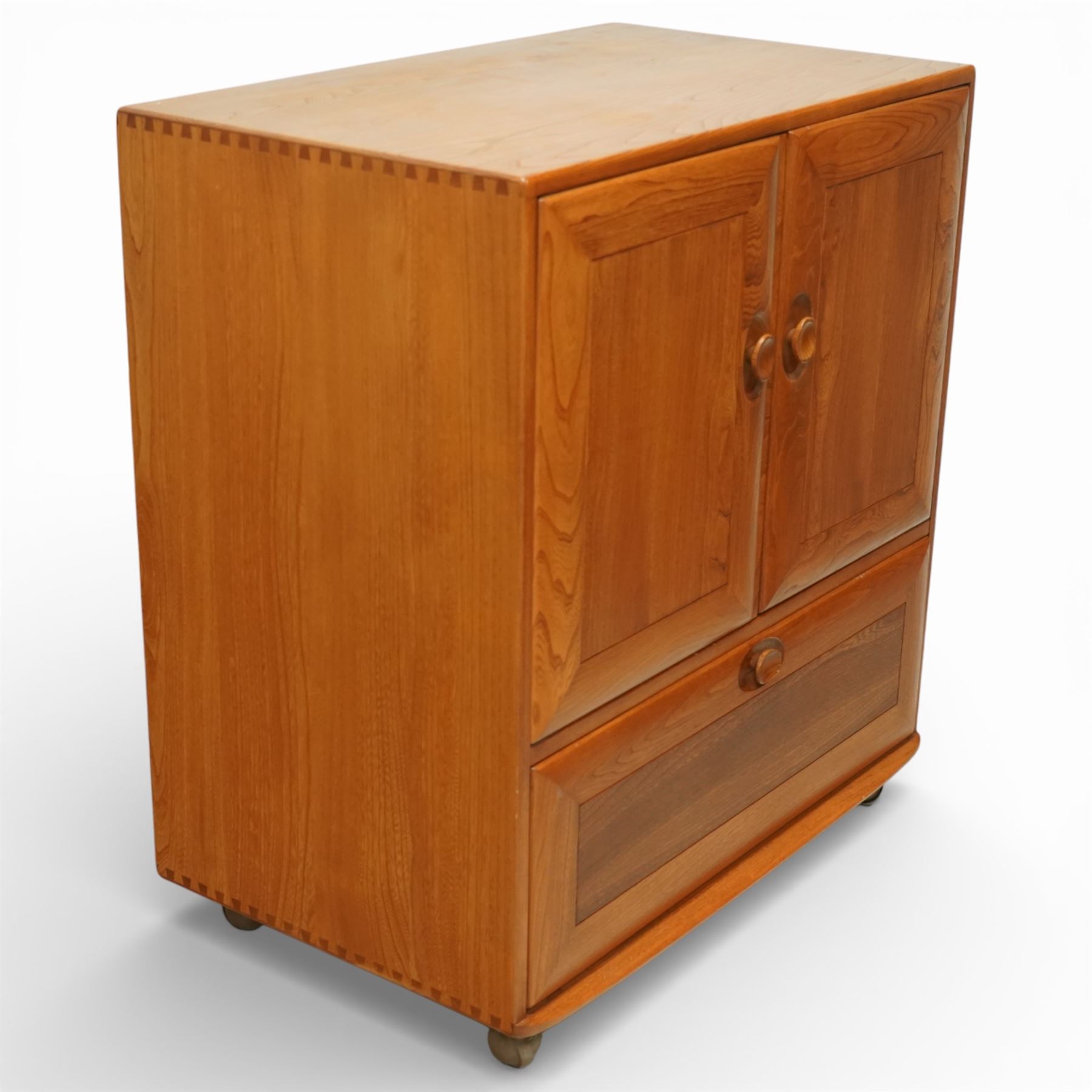 Ercol - elm television cabinet, rectangular top with chamfered edges, fitted with a pair of fielded panel cupboard doors with recessed oval pulls, opening to reveal an adjustable shelf and open back for cables, the lower section with drop-front compartment fitted with record slots and wire dividers, raised on concealed castors