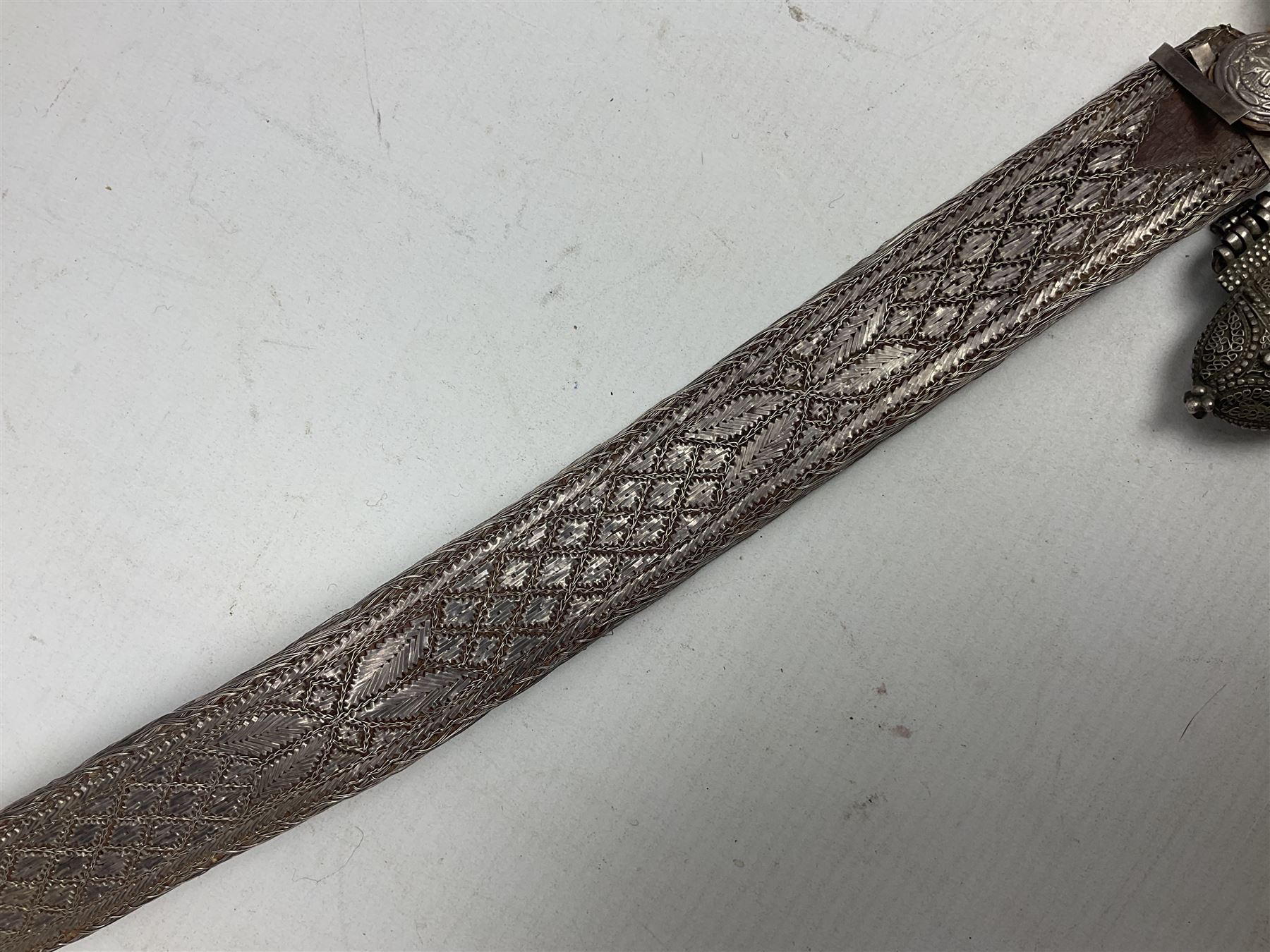 Omani Khanjar dagger, the 19cm curved blade with pronounced medial rib to either side, waisted hilt with dome shaped pommel and silver covered horn grip decorated with filigree bands, floral motifs and beadwork; in an intricately filigree decorated silver and leather scabbard with silver rings woven into the belt mount and fitted with original silver thread-work belt L34cm overall belt length 94cm