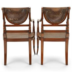 Pair of Sheraton Revival painted mahogany open armchairs, scrolled cresting rail with floral painted decoration over a double-caned back and rose-branch painted back bar, cane seat over C-scroll-painted seat rail, on splayed tapering supports, with all-over painted ebony faux stringing