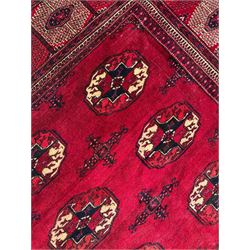 Afghan Bokhara red ground carpet, the field decorated with four rows of Gul motifs interspersed with Hac motifs, the border with lattice pattern panels within small geometric guard stripes, geometric patterned end panels