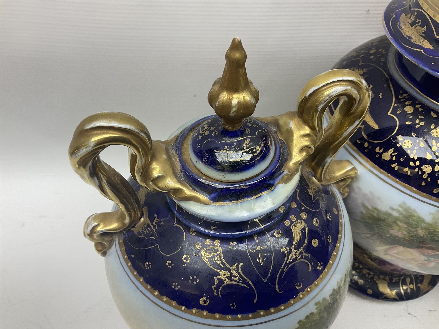 19th century Vienna style porcelain 'Musik' garniture, the central vase of baluster form with domed cover flanked by two smaller vases with twin curved gilt handles to short neck, each decorated with classical figural vignettes between blue borders heightened with gilt, H33.5cm