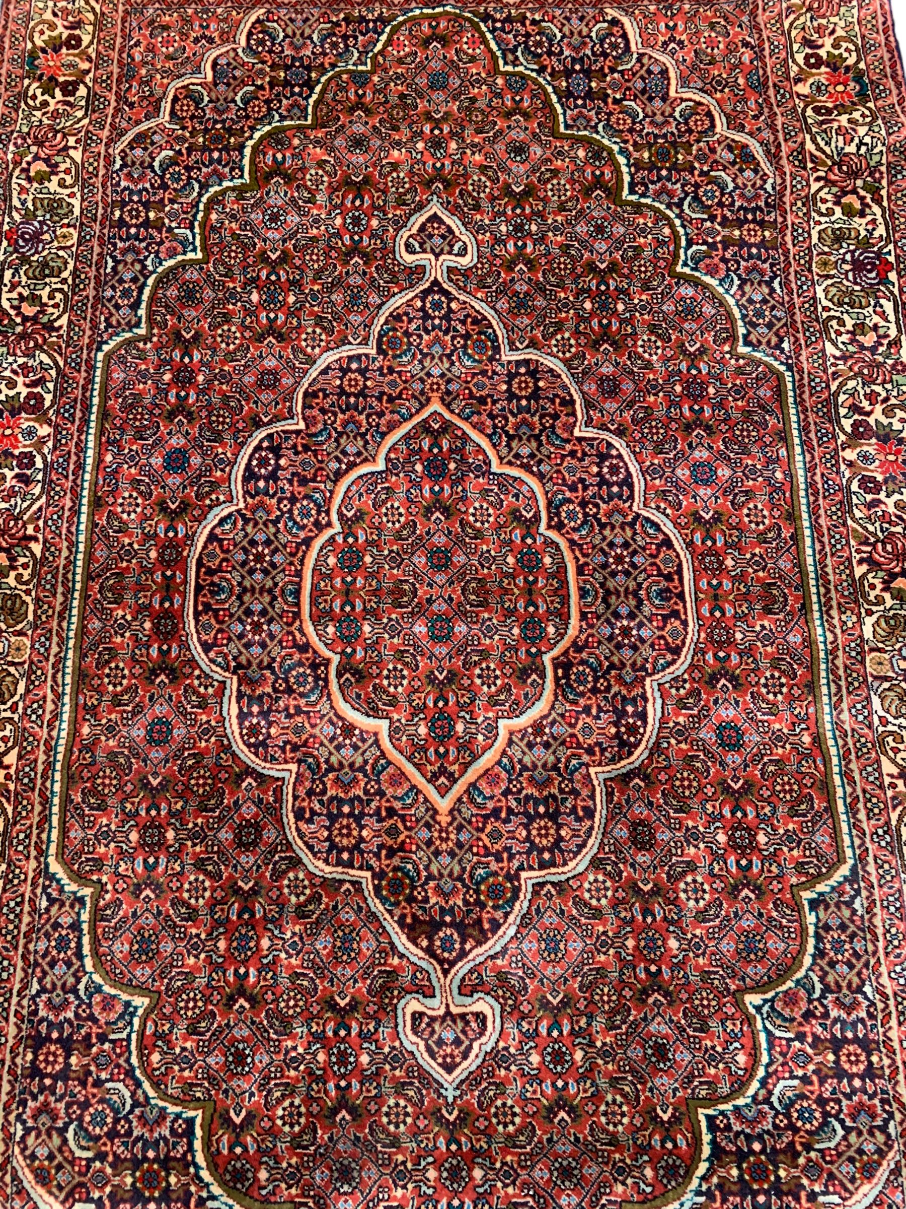 Persian Bidjar crimson ground rug, thick woollen pile, the field decorated with repeating Herati motifs within cusped outlines, the guarded border decorated with repeating flower head motifs