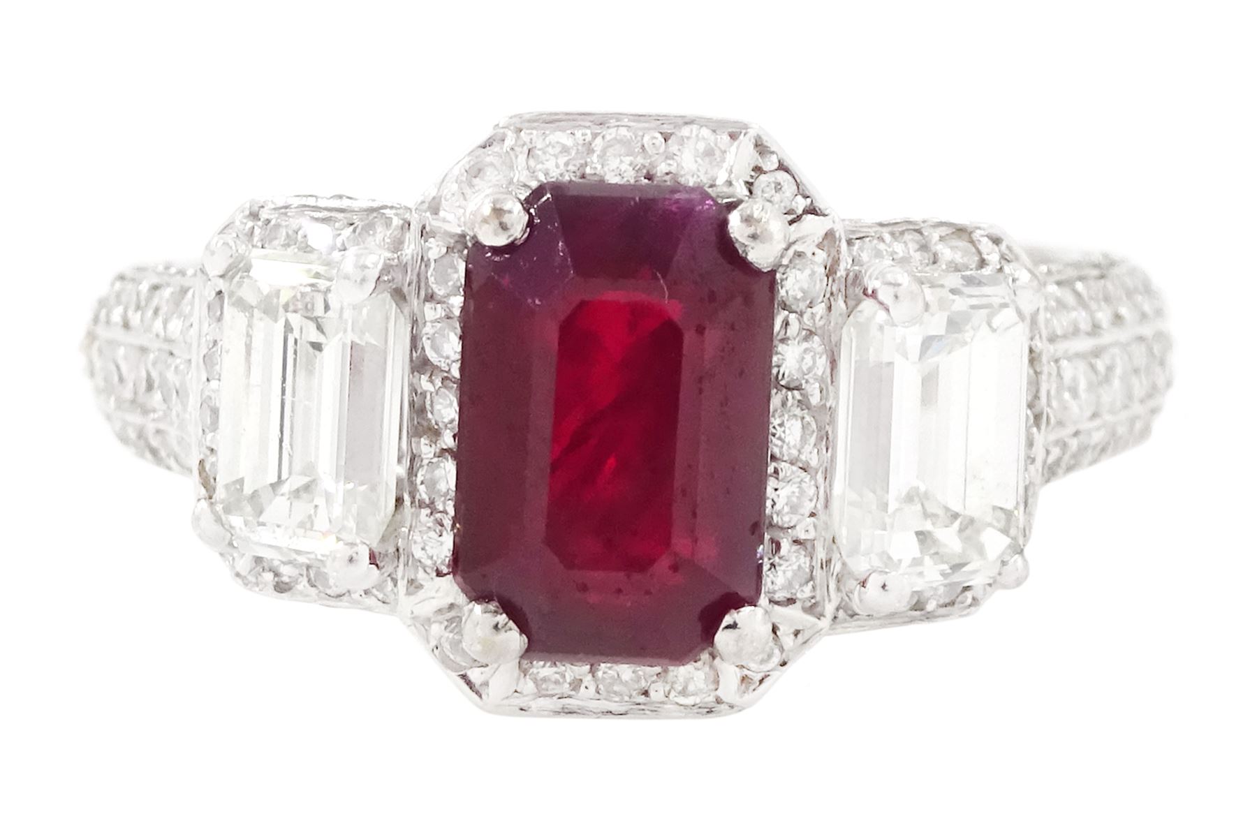 18ct white gold ruby and diamond trilogy ring, single emerald cut ruby of approx 1.85 carat, with a single emerald cut diamond set either side, all surrounded by round brilliant cut diamonds, the shoulders set with three rows of round brilliant cut diamonds, principal two emerald cut diamonds approx 1.10 carat