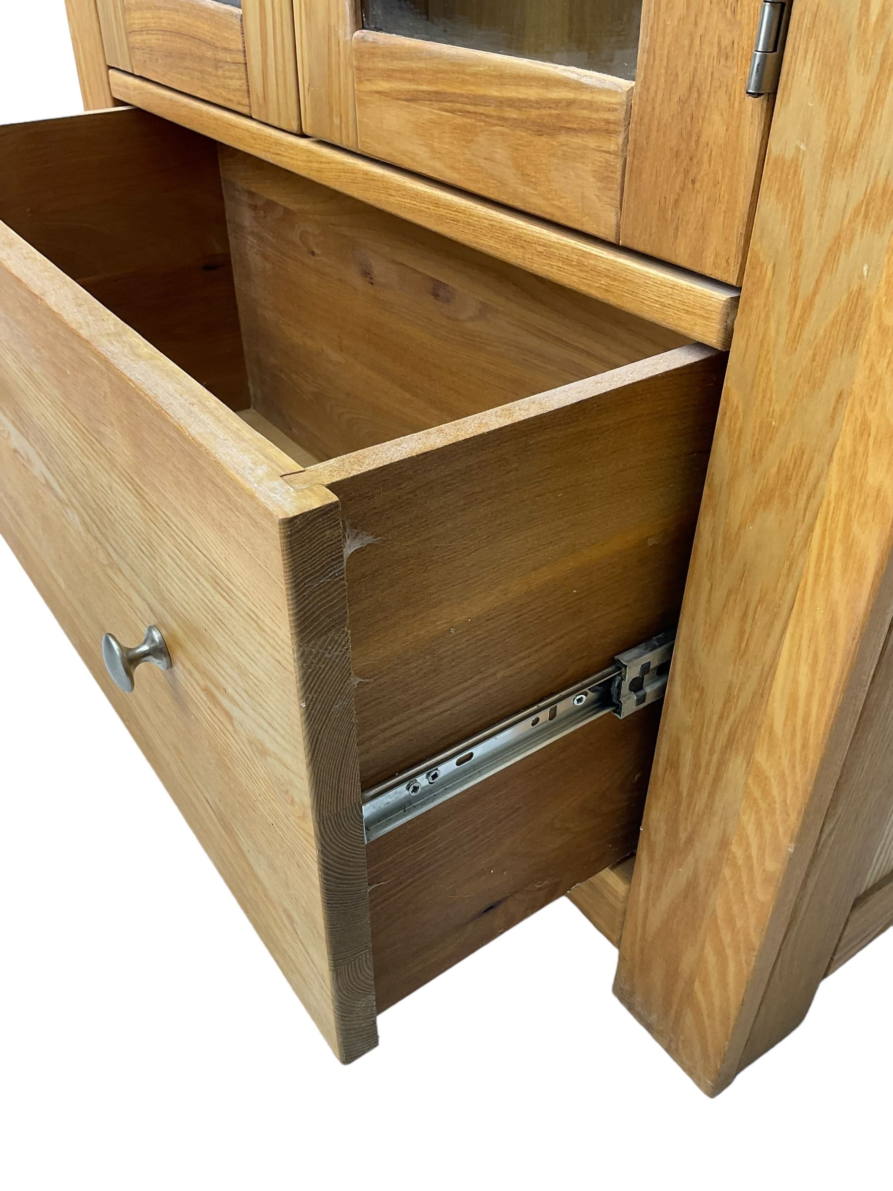 Light oak bookcase display cabinet, projecting square cornice over glazed double doors enclosing three adjustable shelves, single drawer base, on stile supports