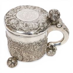 Northern European silver peg tankard, probably late 18th/early 19th century, of cylindrical form, the body repoussé decorated with scrolling and blossoming acanthus, fitted with scroll handle with shield terminal, the hinged cover with conforming repoussé decoration surrounding a central circular panel engraved with monogram beneath initials EASBGD, opening with ball thumbpiece detailed with fruits, raised upon three confirming ball feet mounted with shaped panels also detailed with fruits, bearing indistinct mark beneath, H19cm
