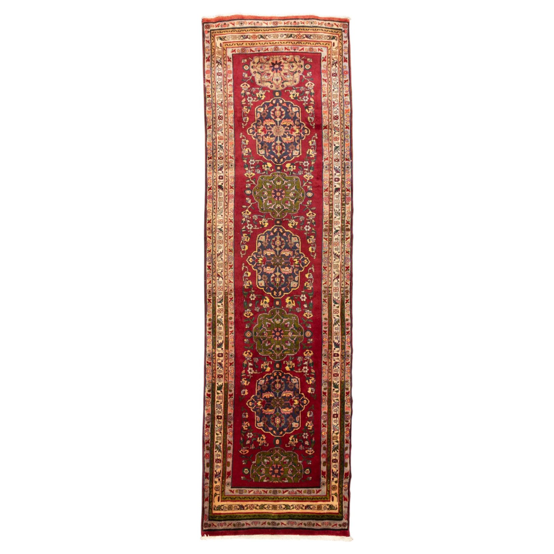 North West Persian Tariz hand-knotted runner, madder red field with a column of linked lozenge medallions in shades of indigo blue and pistachio green framed by stylized floral motifs within triple borders of rosettes and scrolling vines on an ivory ground, with cotton fringe ends
