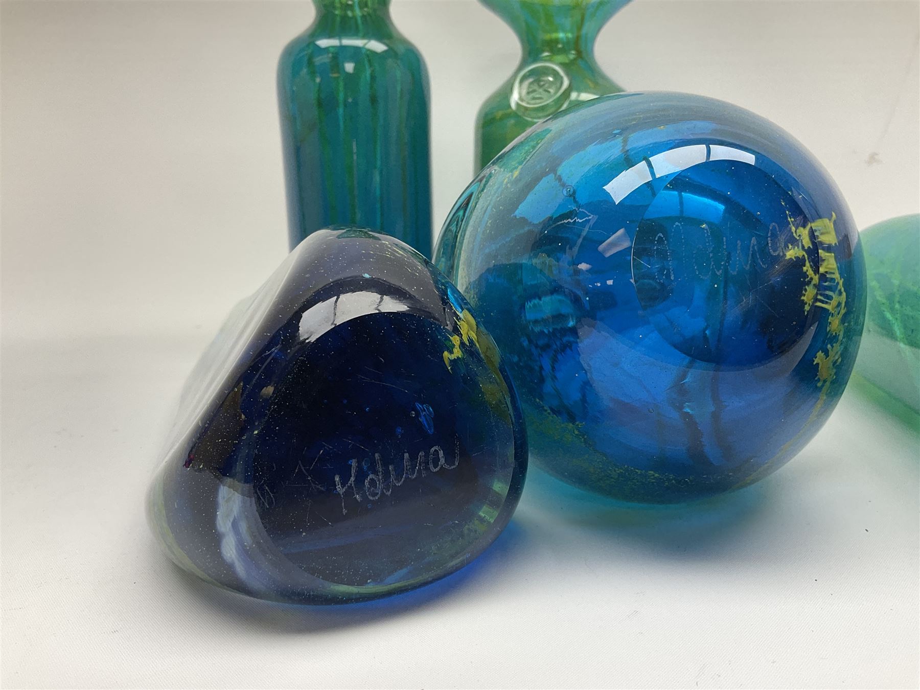 Quantity of M’dina art glass to include a streaked blue and green bottle form vase with captured bubble design and slender neck, H35cm, along with a paperweight, ovoid form vase and another vase all decorated in a blue, brown and white colour way, other contemporary glass examples etc with etched marks beneath